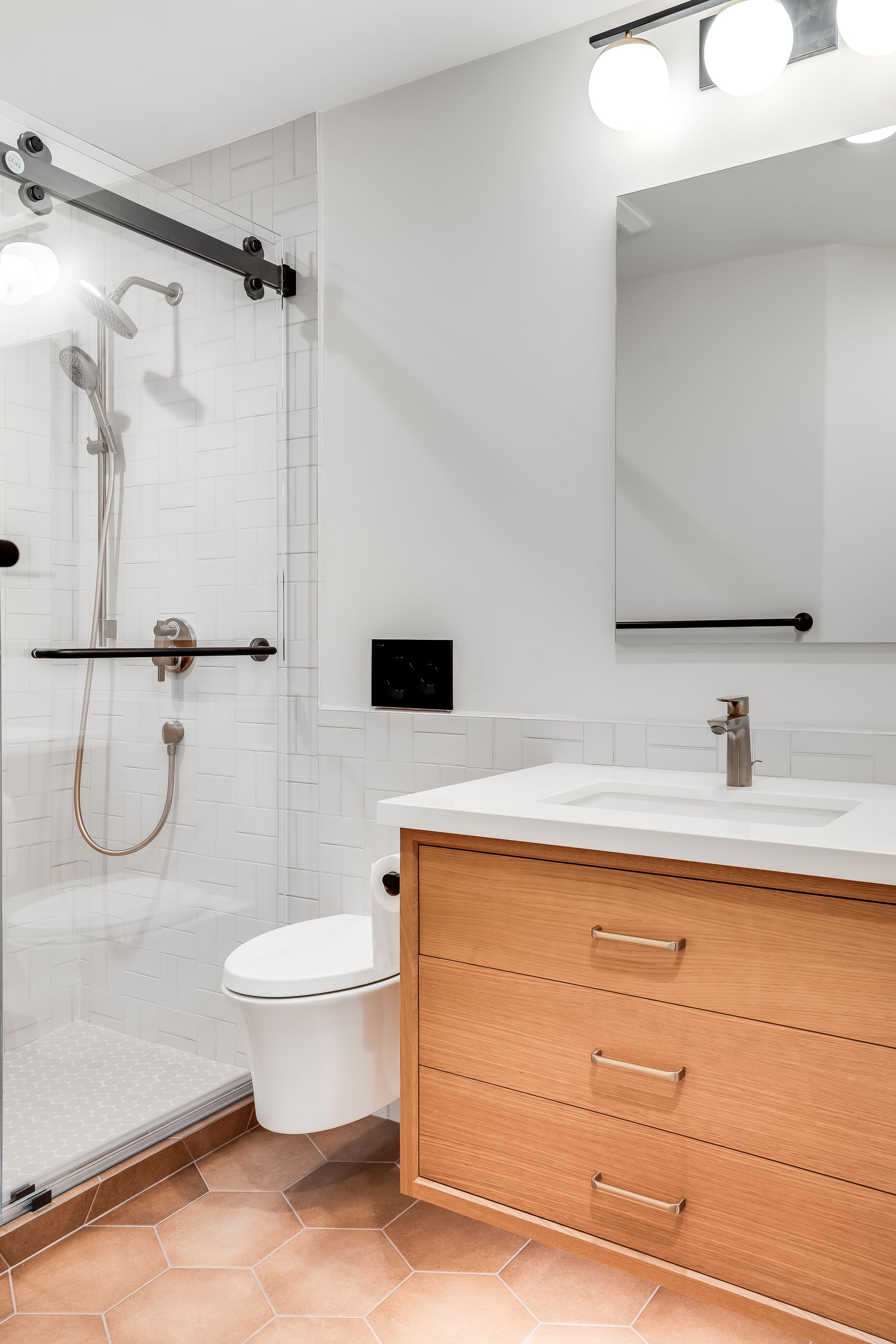 Modern bathroom with glass shower, toilet, wood vanity, white sink, and large mirror