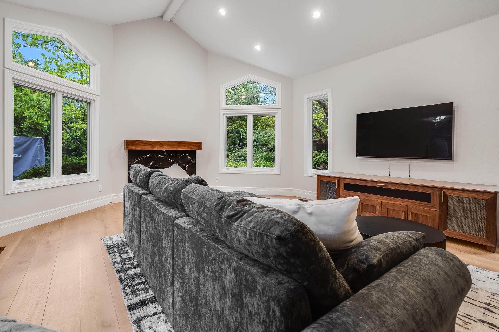 Bright living room with gray sectional, fireplace, large windows, and wall-mounted TV
