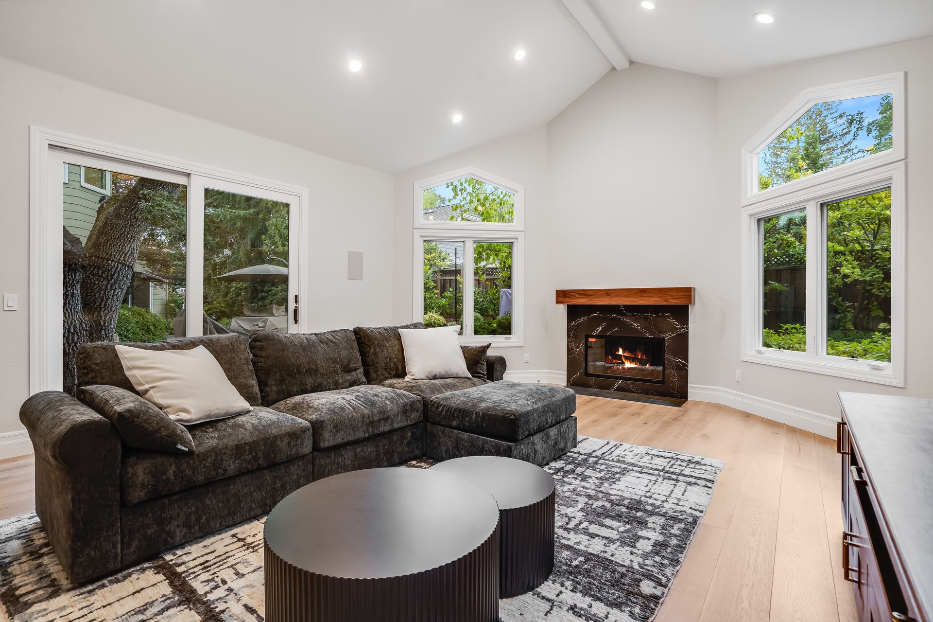 Bright modern living room with gray sofa, round coffee table, fireplace, and large windows