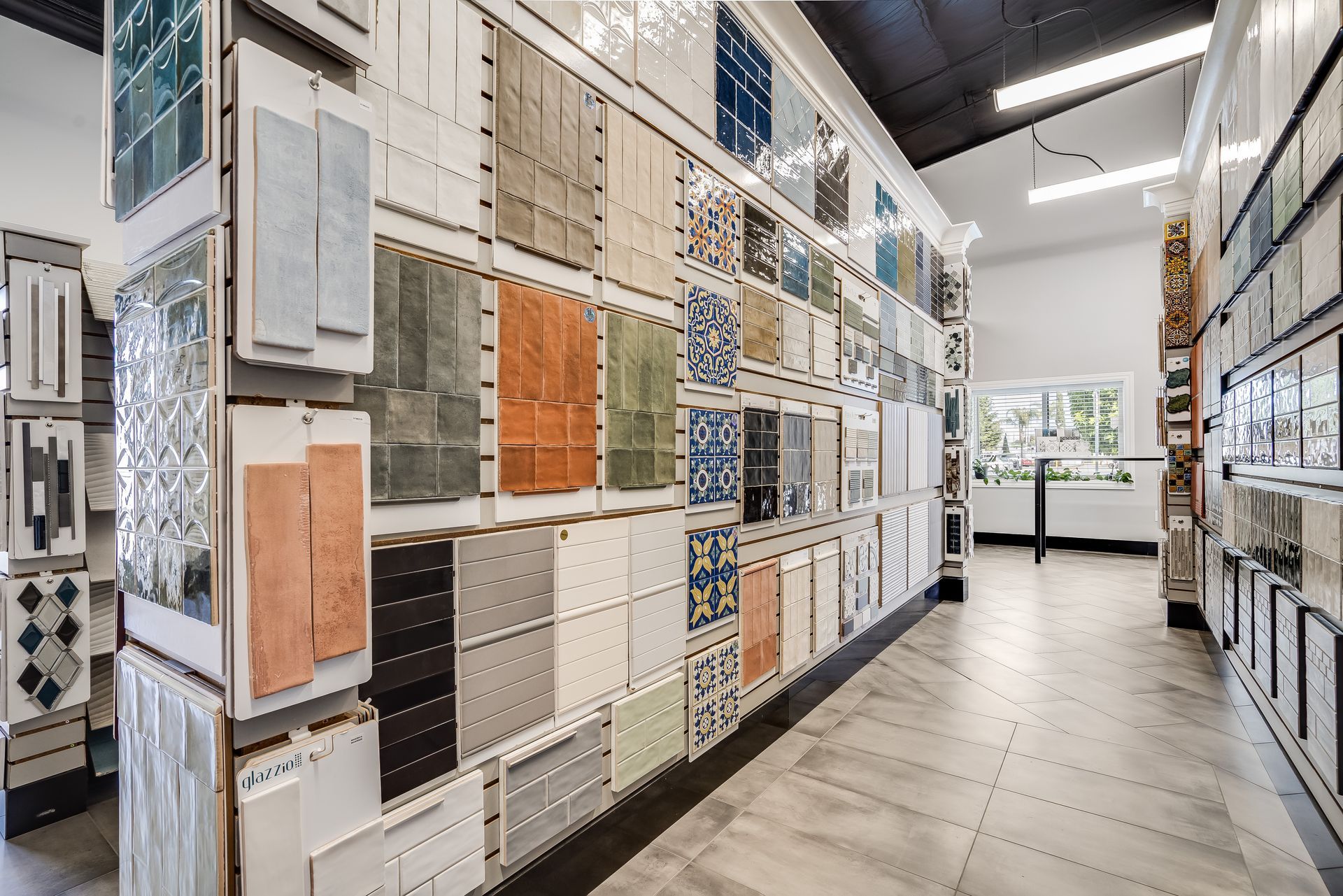 Tile showroom aisle with wall displays of patterned and textured tiles in neutral and blue tones