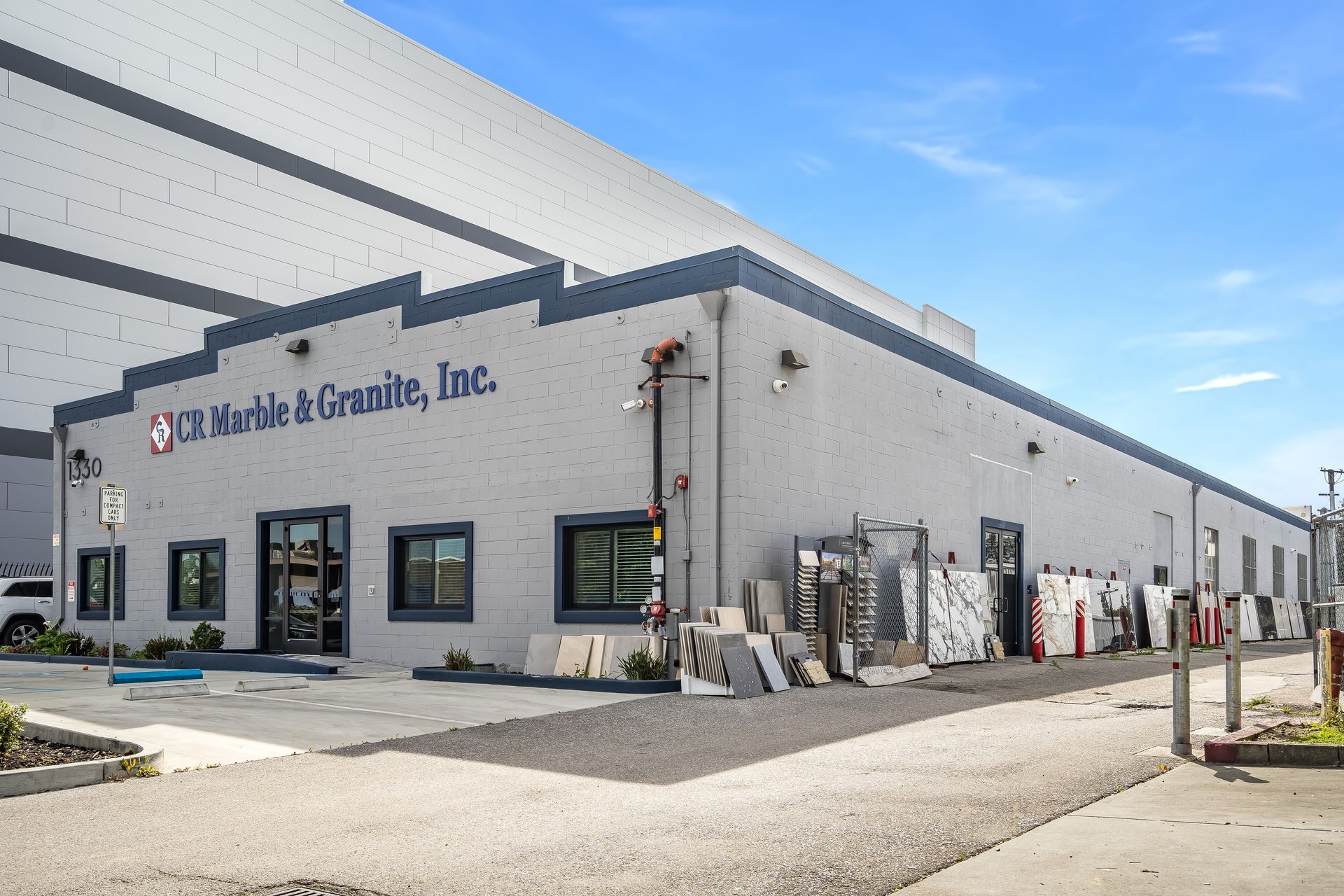 Gray industrial building with Stone Granite, Inc. sign, pallets and stone slabs outside on a sunny day