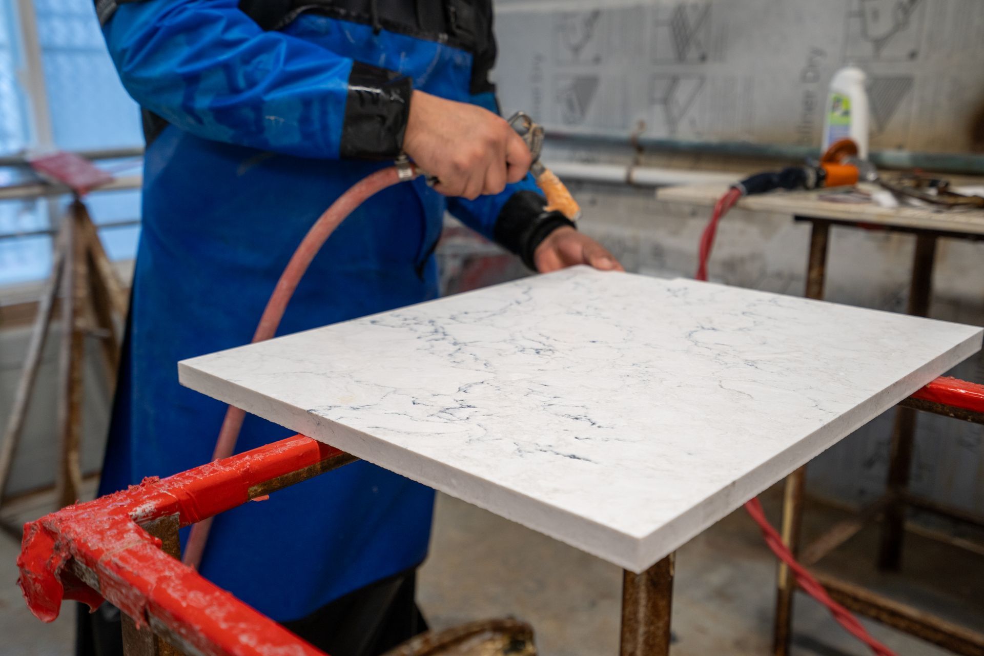 Worker in blue coat sanding a white countertop on a workshop table.