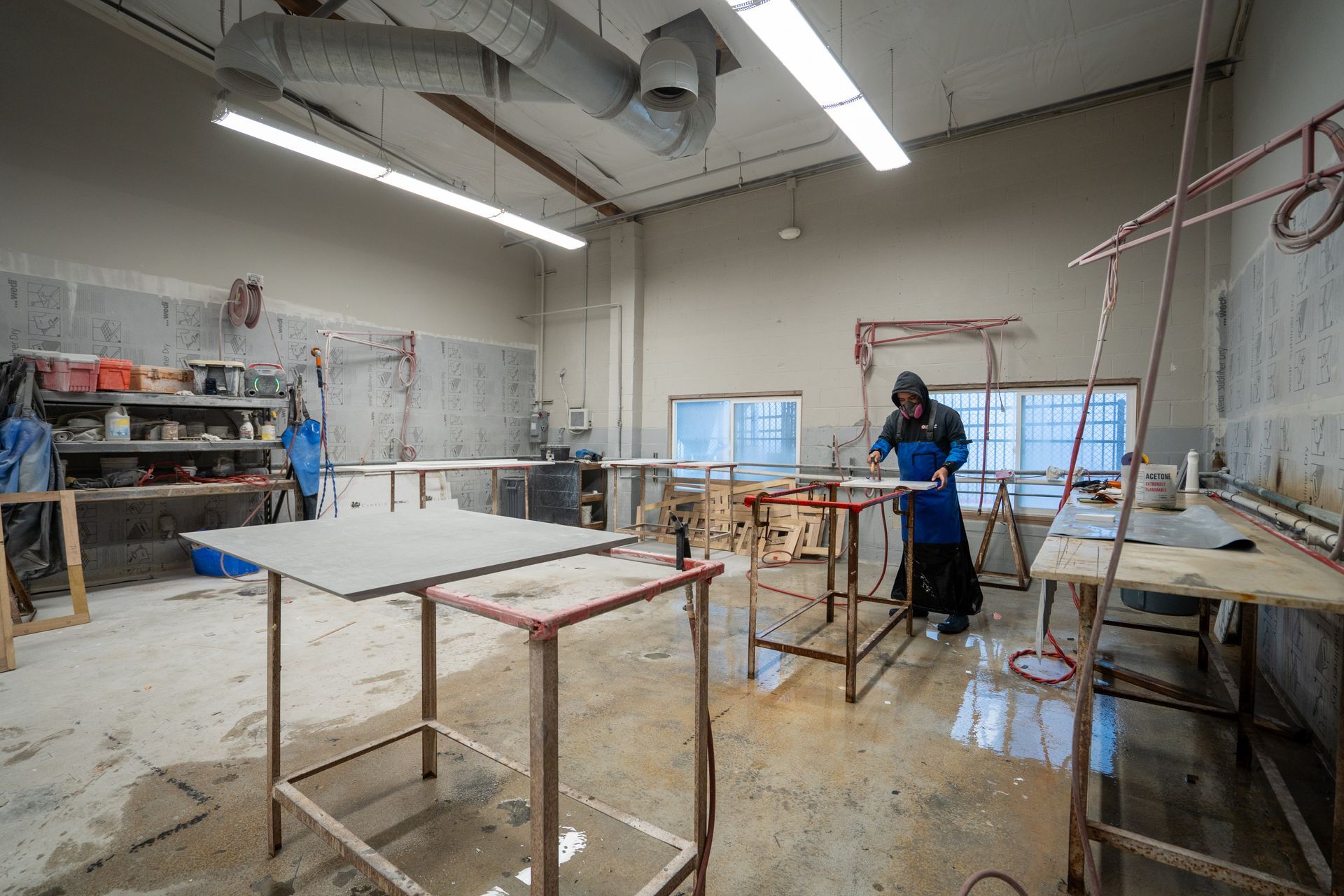 Spacious workshop with tables, tools, and a person working near a metal frame.