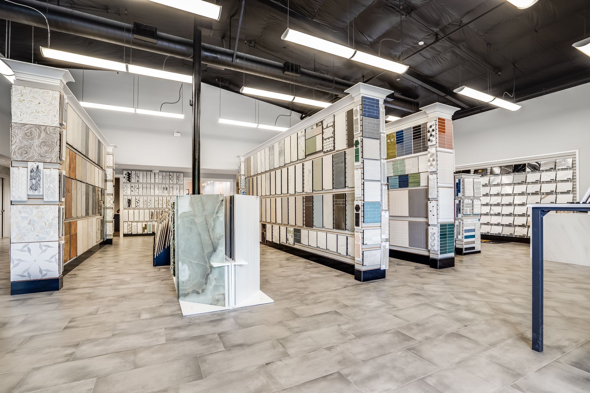 Spacious tile showroom with rows of display panels and samples under bright warehouse lighting.