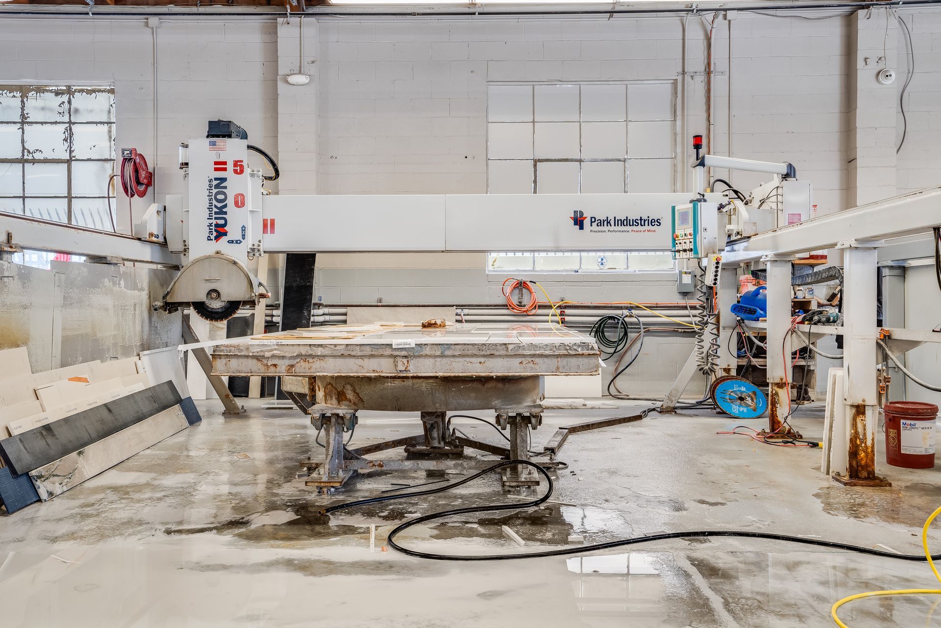 Large industrial CNC machine in a workshop, with a central worktable and scattered tools on the floor.