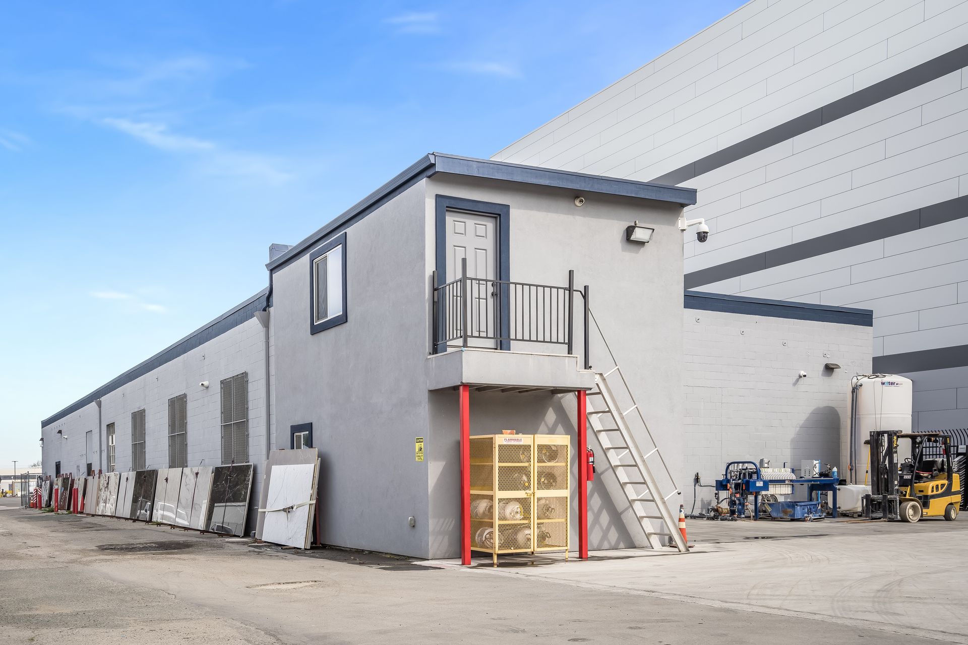 Gray industrial building with outdoor stairs, loading doors, and equipment in a warehouse yard