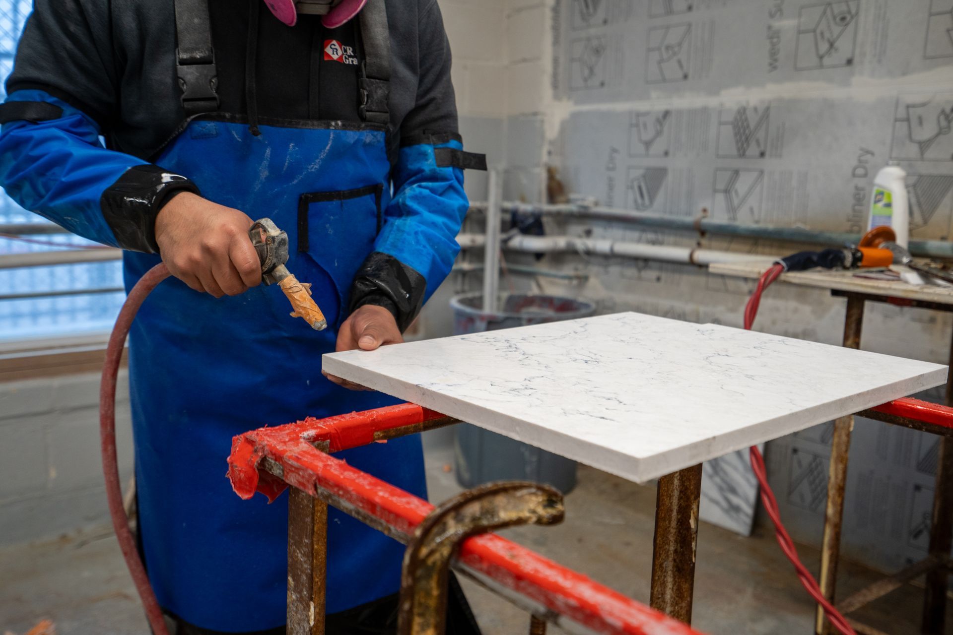 Worker in blue overalls cutting a white tile on a wet saw in a workshop
