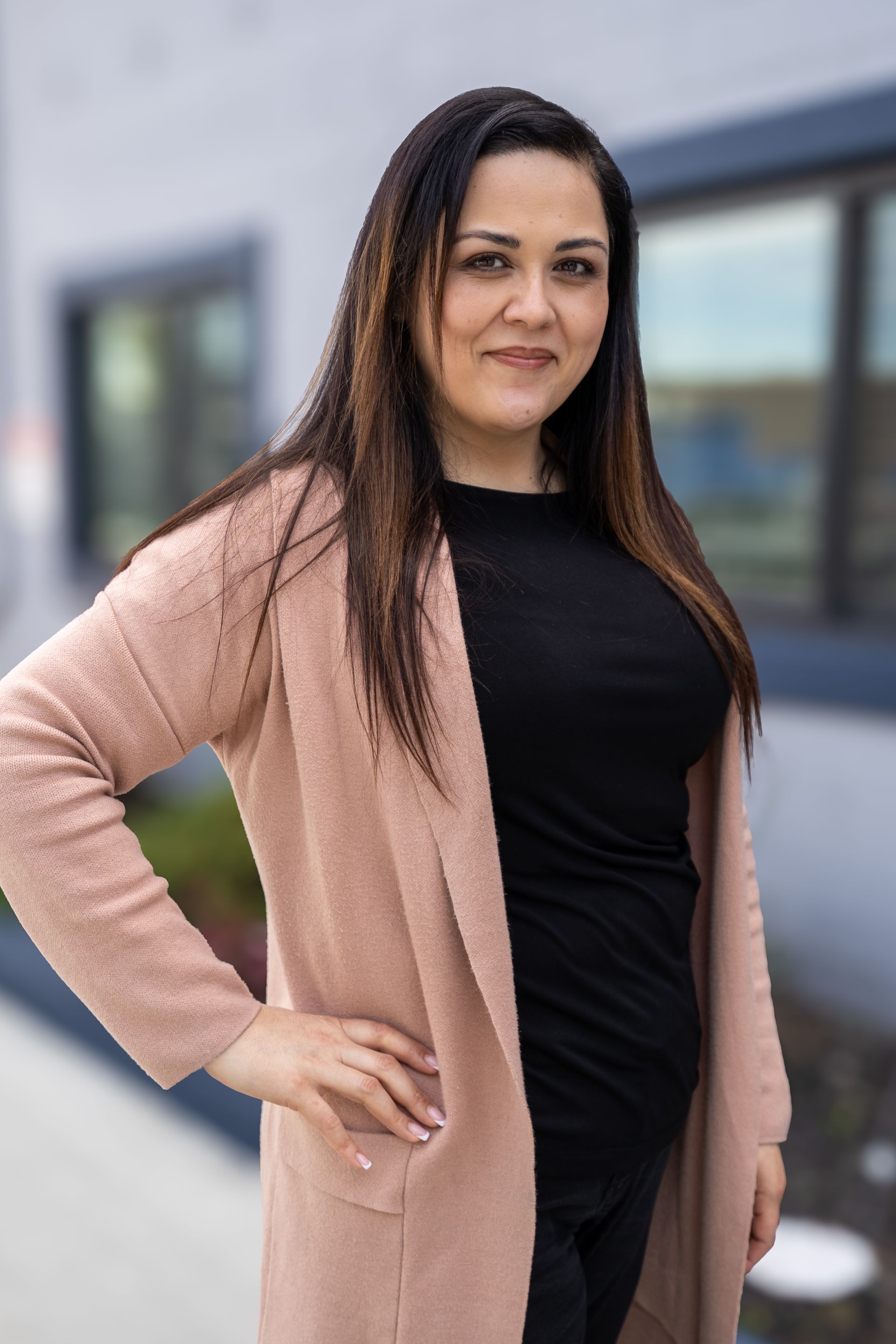 Woman standing outdoors with hand on hip, wearing a black top and beige cardigan.