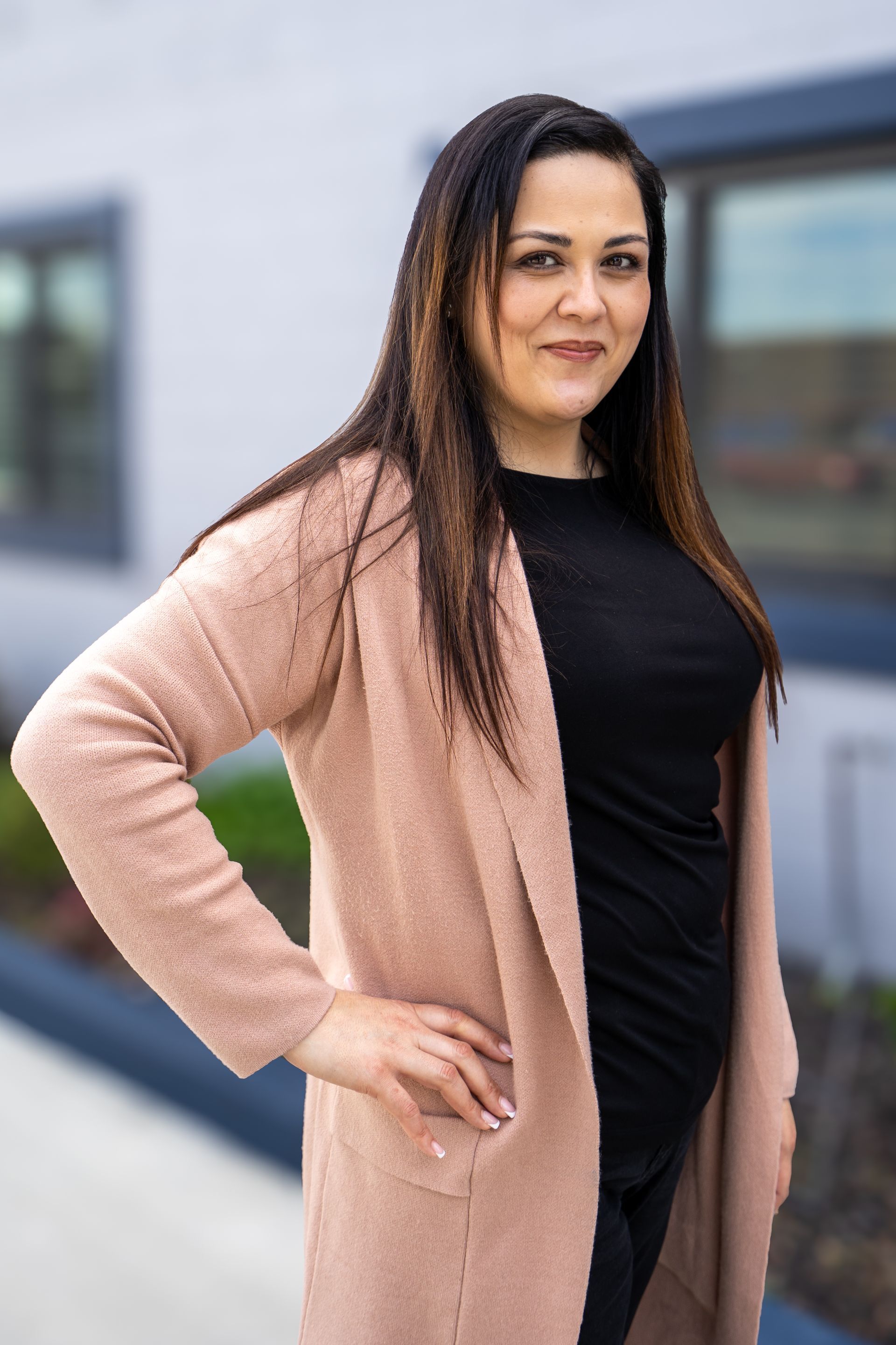 Woman in a pink cardigan and black top standing outdoors with one hand on her hip.