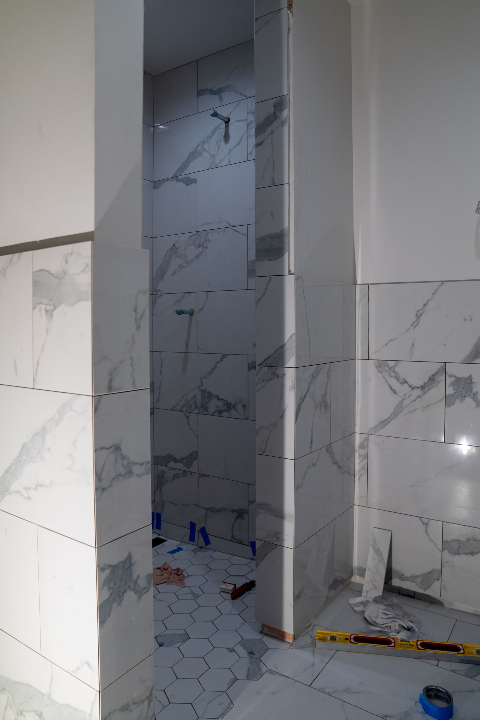 Partially tiled bathroom with marble-look wall tiles and a shower area under construction