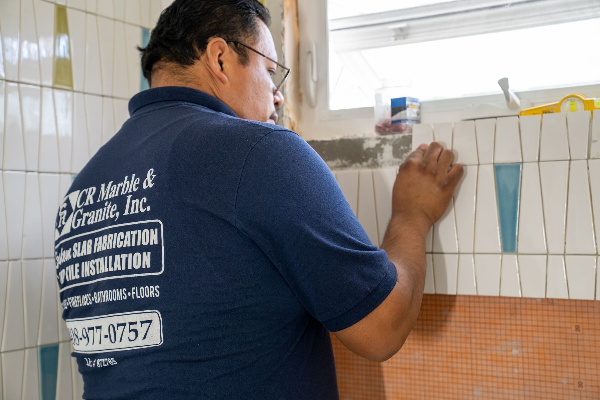 Worker in navy shirt applying white tile grout on a bathroom wall.