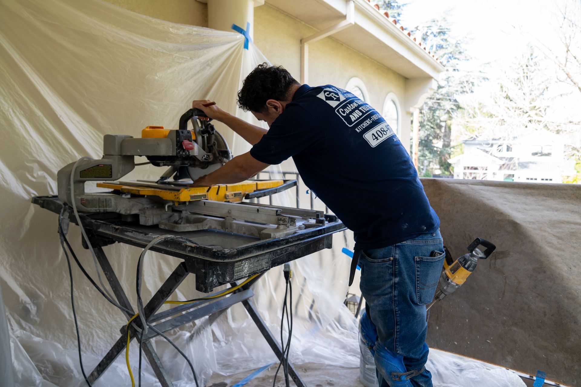 Worker cutting material on a table saw in a tarp-covered outdoor work area