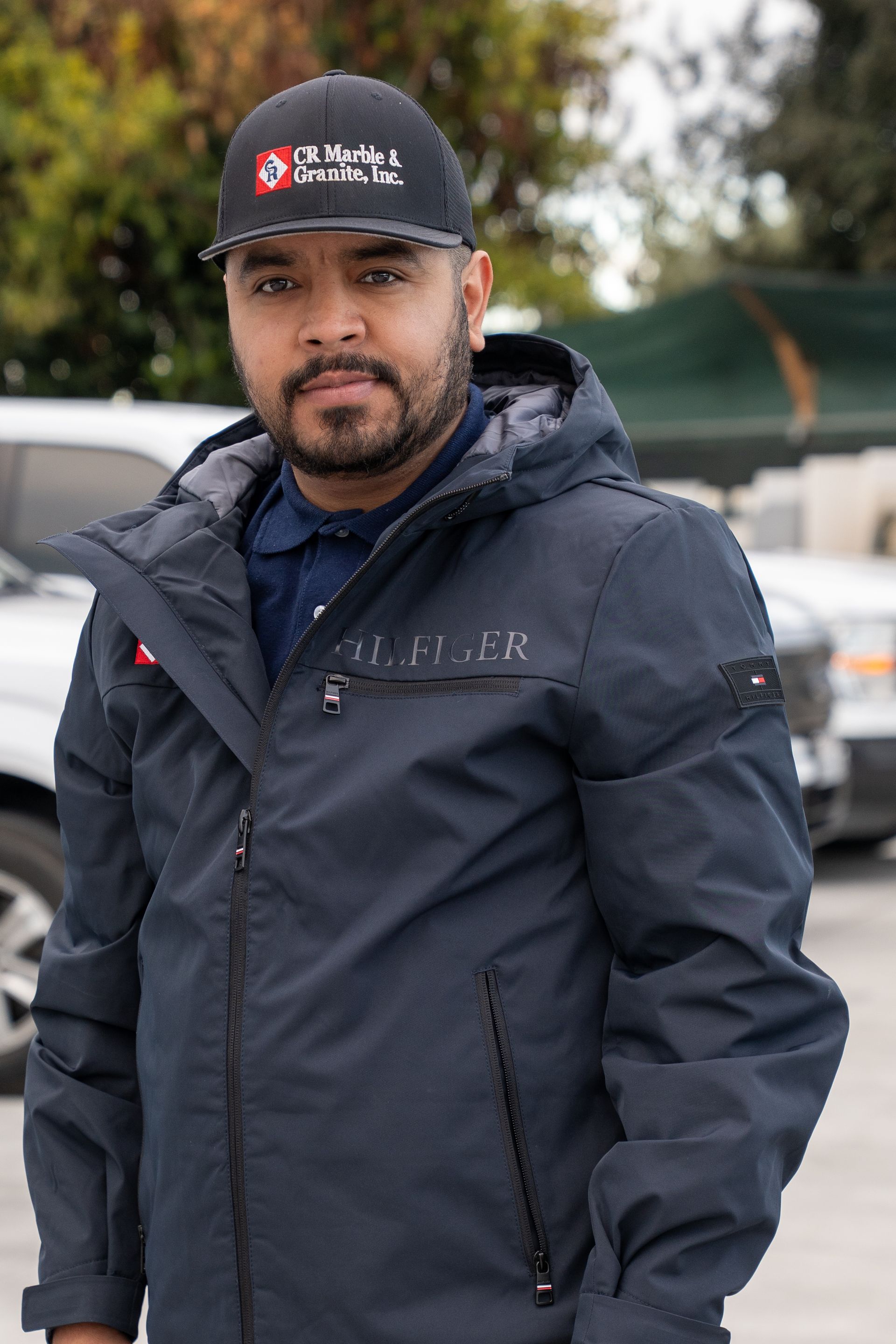 Man in a navy jacket and black cap standing outdoors in a parking lot