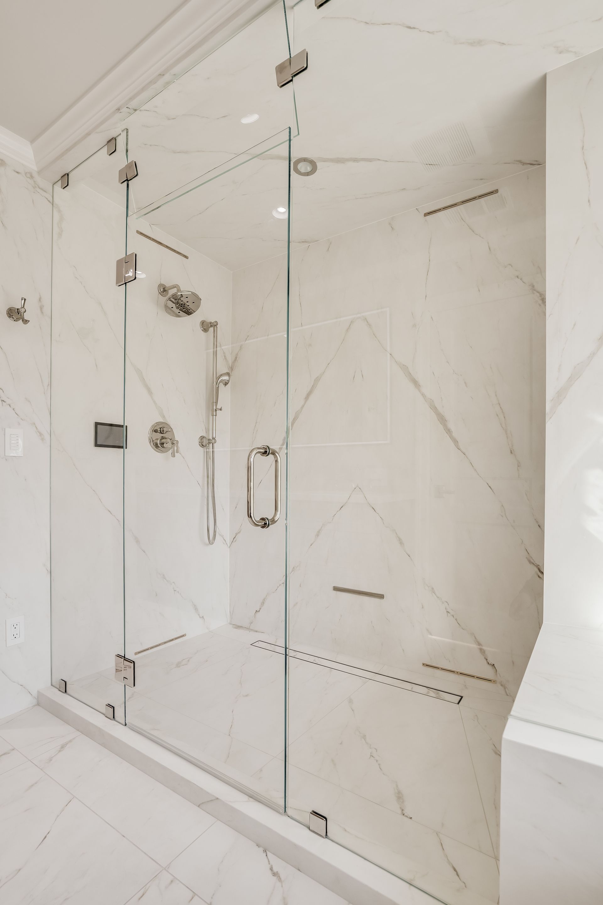 Glass shower enclosure in a white marble bathroom with chrome hardware and shower fixtures.
