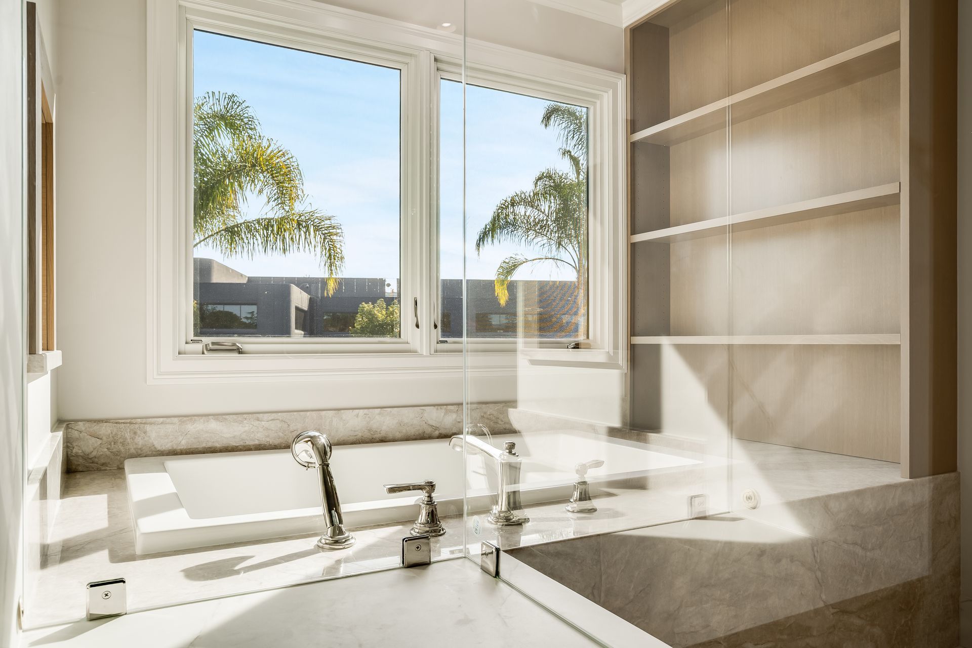 Bright bathroom with a double sink and large windows showing trees outside.