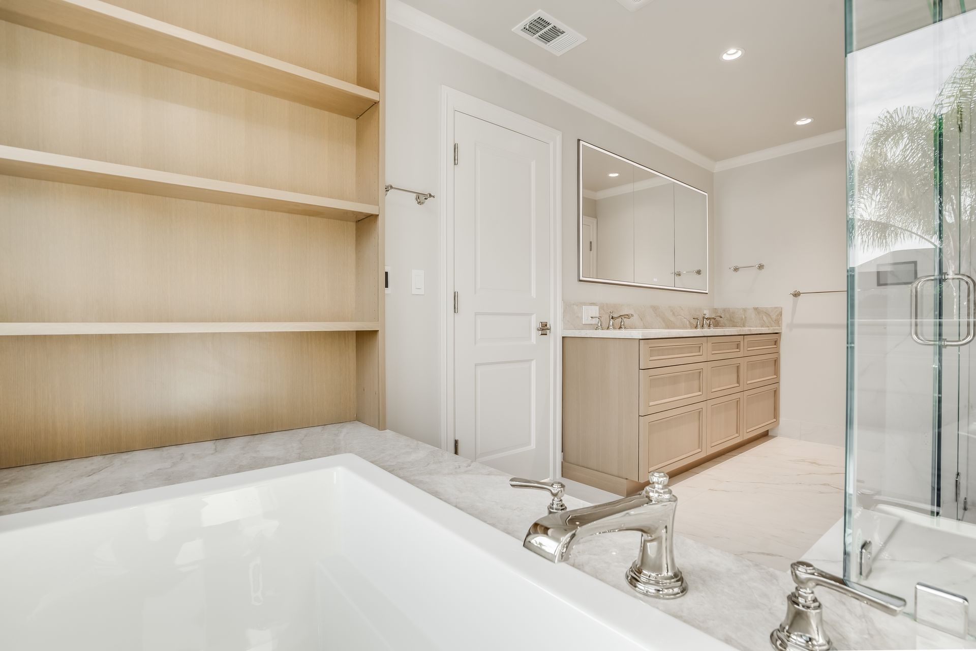 Bright white bathroom with a bathtub, wooden shelves, vanity, mirror, and glass shower enclosure