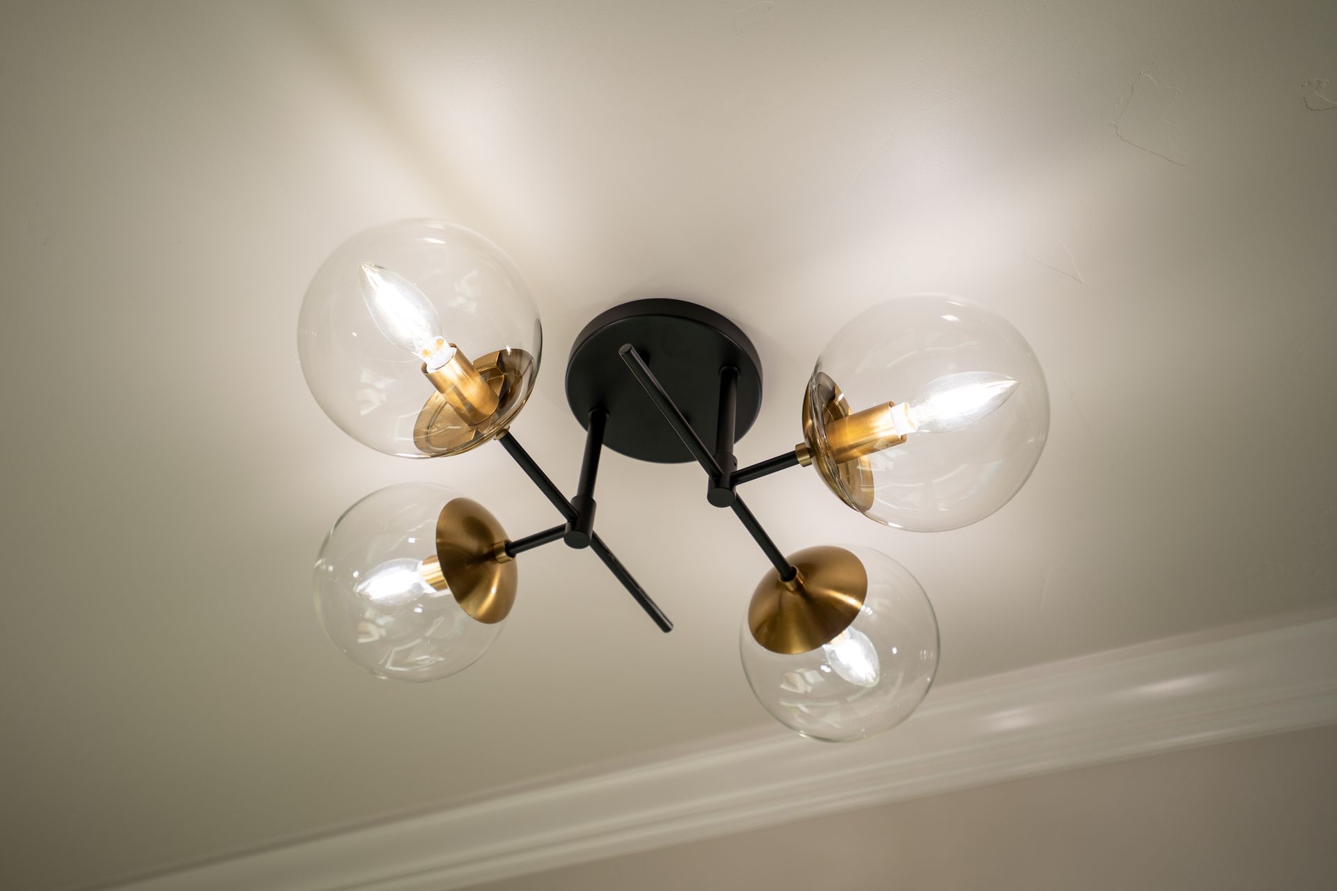 Modern ceiling light with four clear glass globes and brass accents on a white ceiling