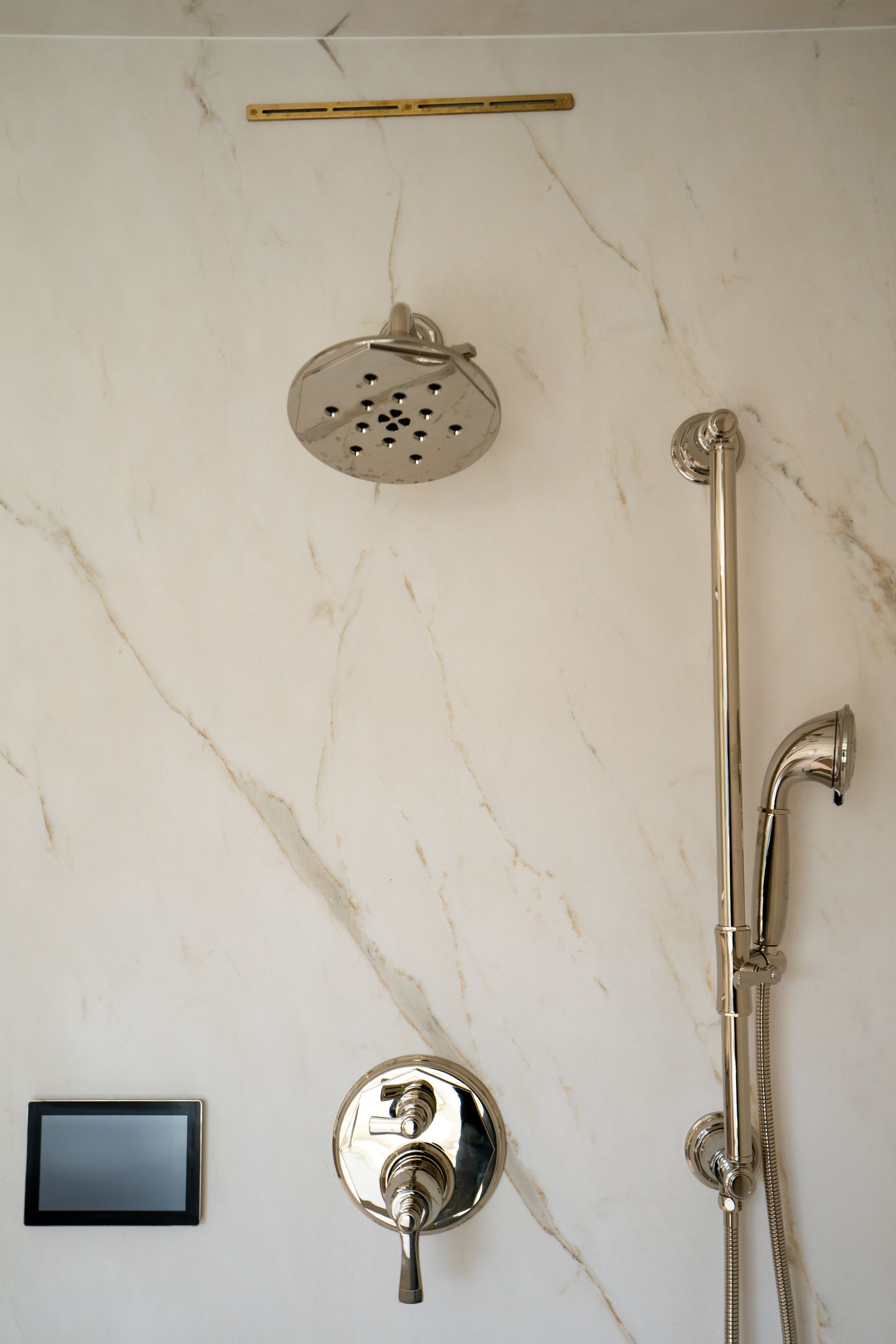 Bathroom shower with rain showerhead, handheld shower, and wall controls on marble tile.