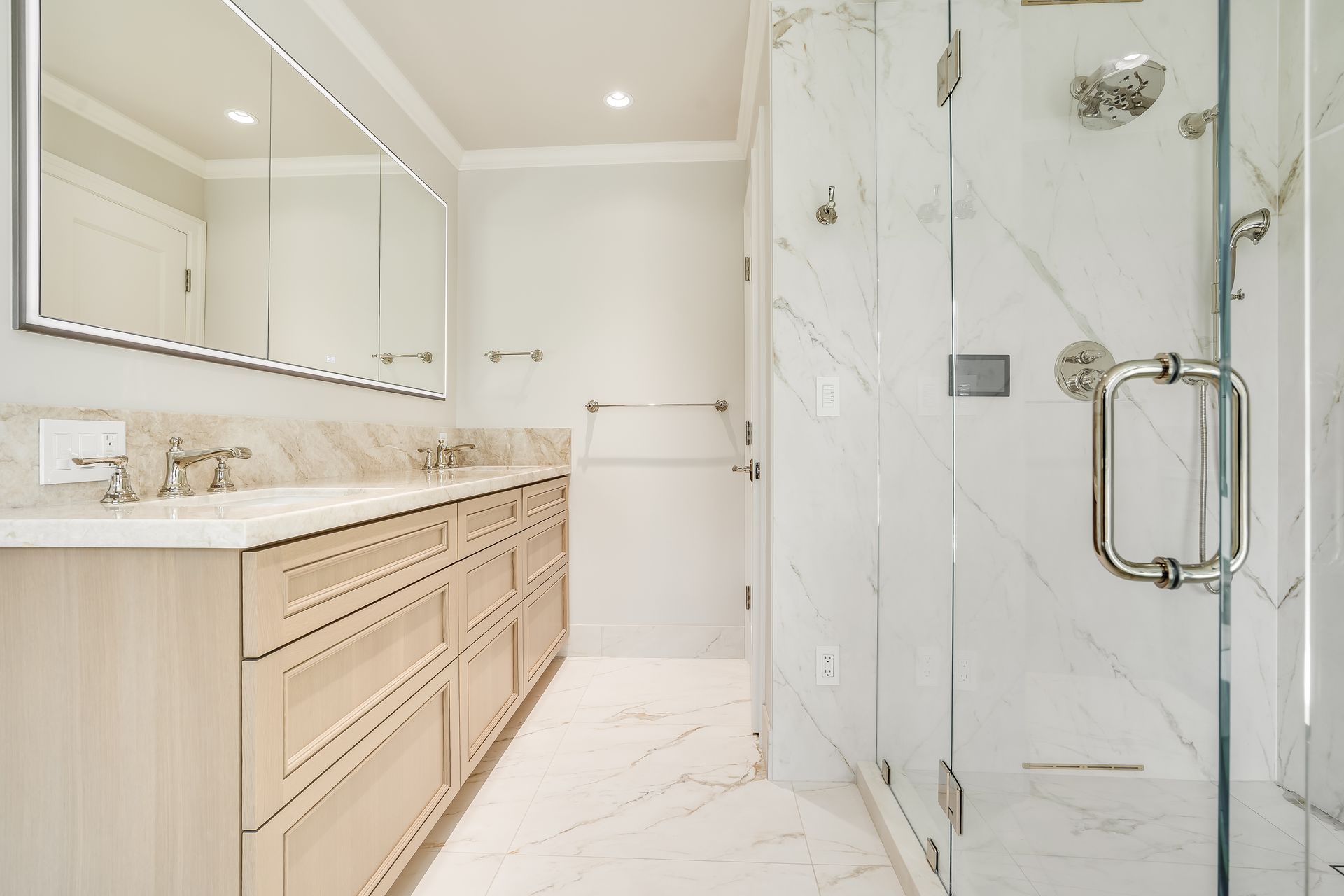 Bright modern bathroom with marble shower, double vanity, and large mirrors