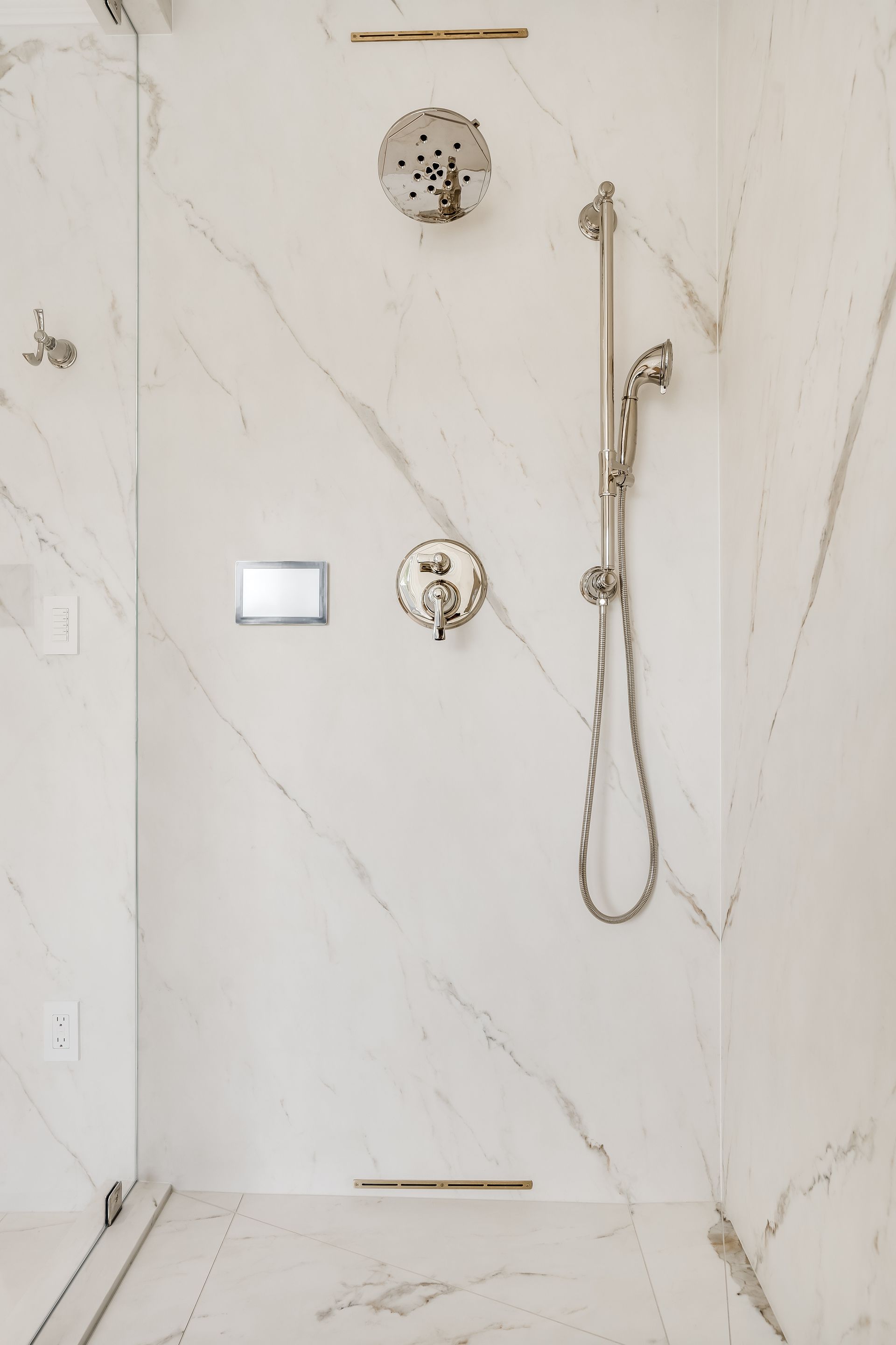White marble-tiled shower with chrome showerhead, controls, and handheld sprayer.