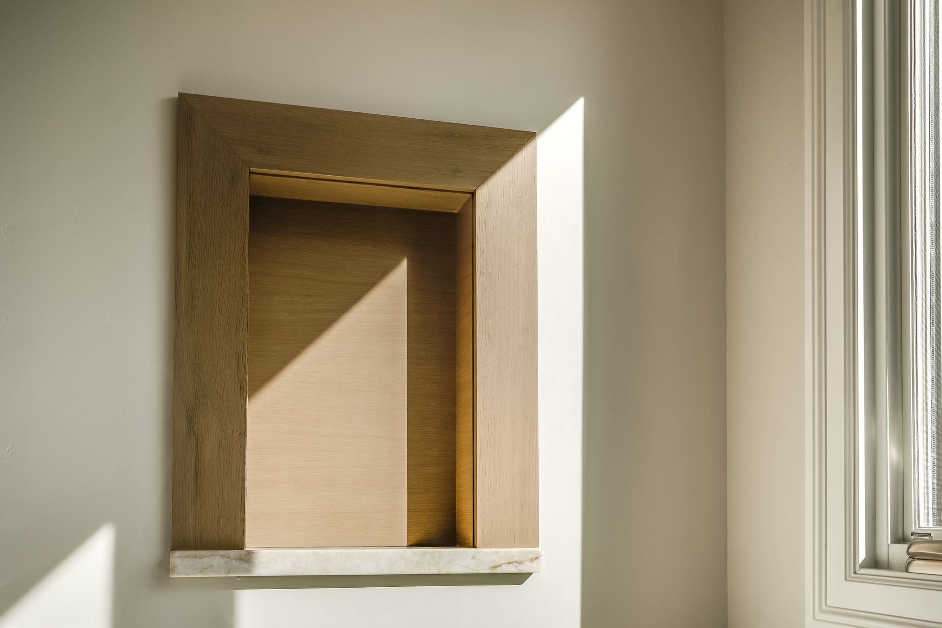 Built-in wall niche with wooden frame in a sunlit room beside a window