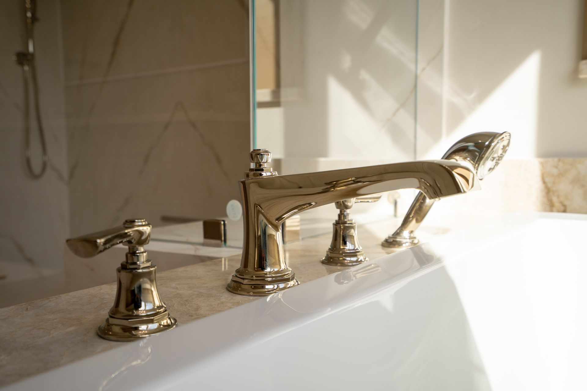 Chrome bathtub faucet and handles on a white tub, lit by sunlight in a bathroom.