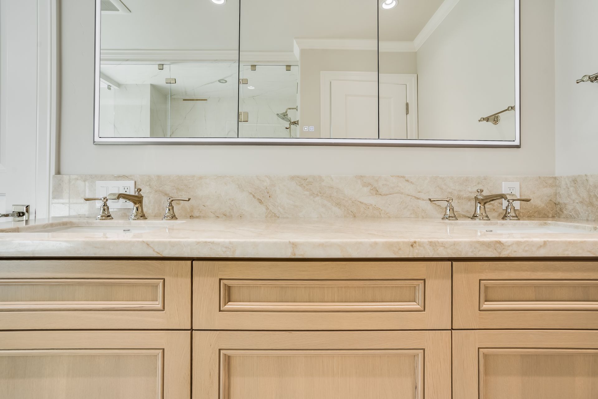 Light wood bathroom vanity with white countertop and large mirror in a bright, neutral bathroom