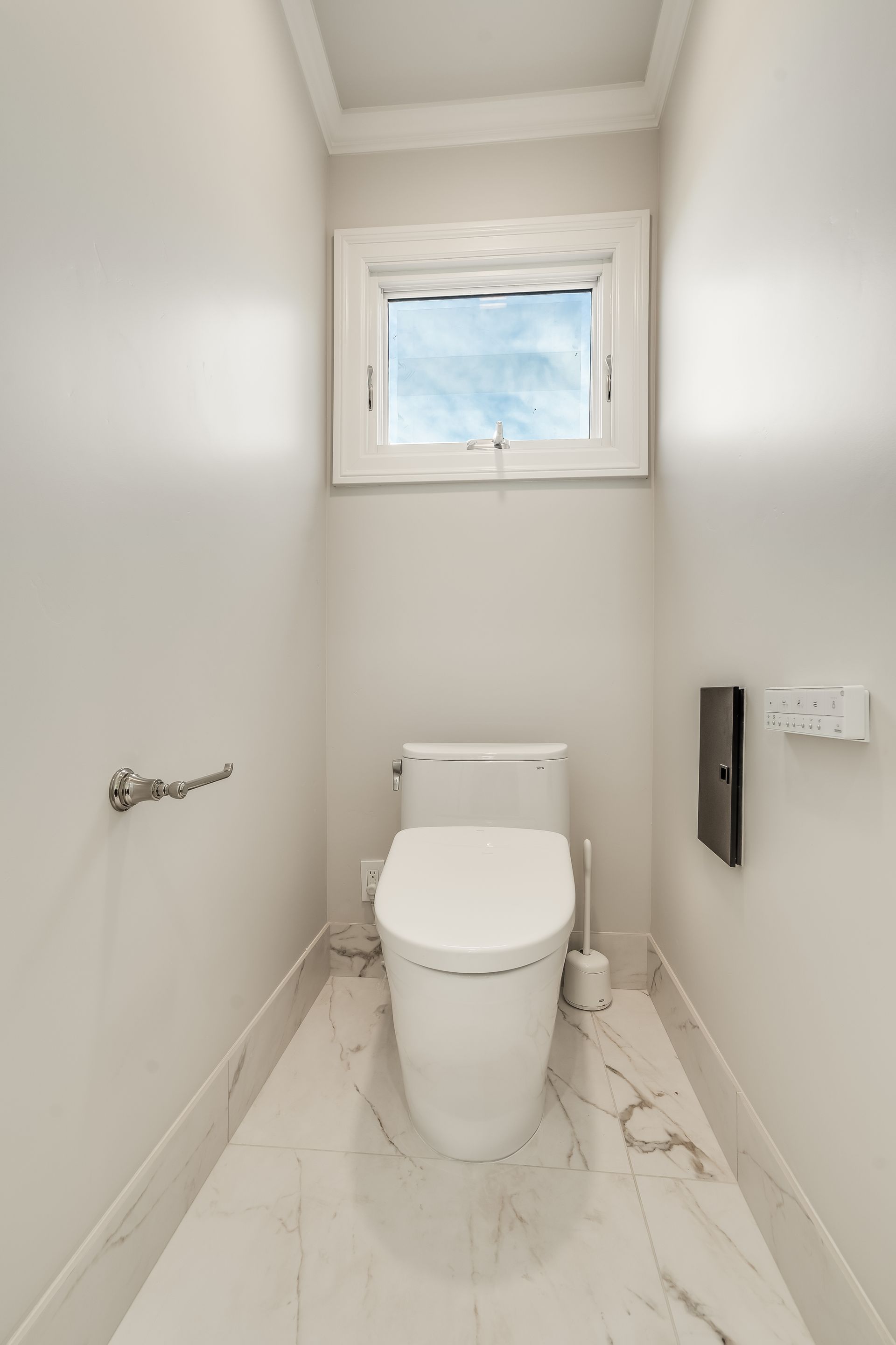 Narrow white toilet room with a toilet, small frosted window, and wall-mounted toilet paper holder.