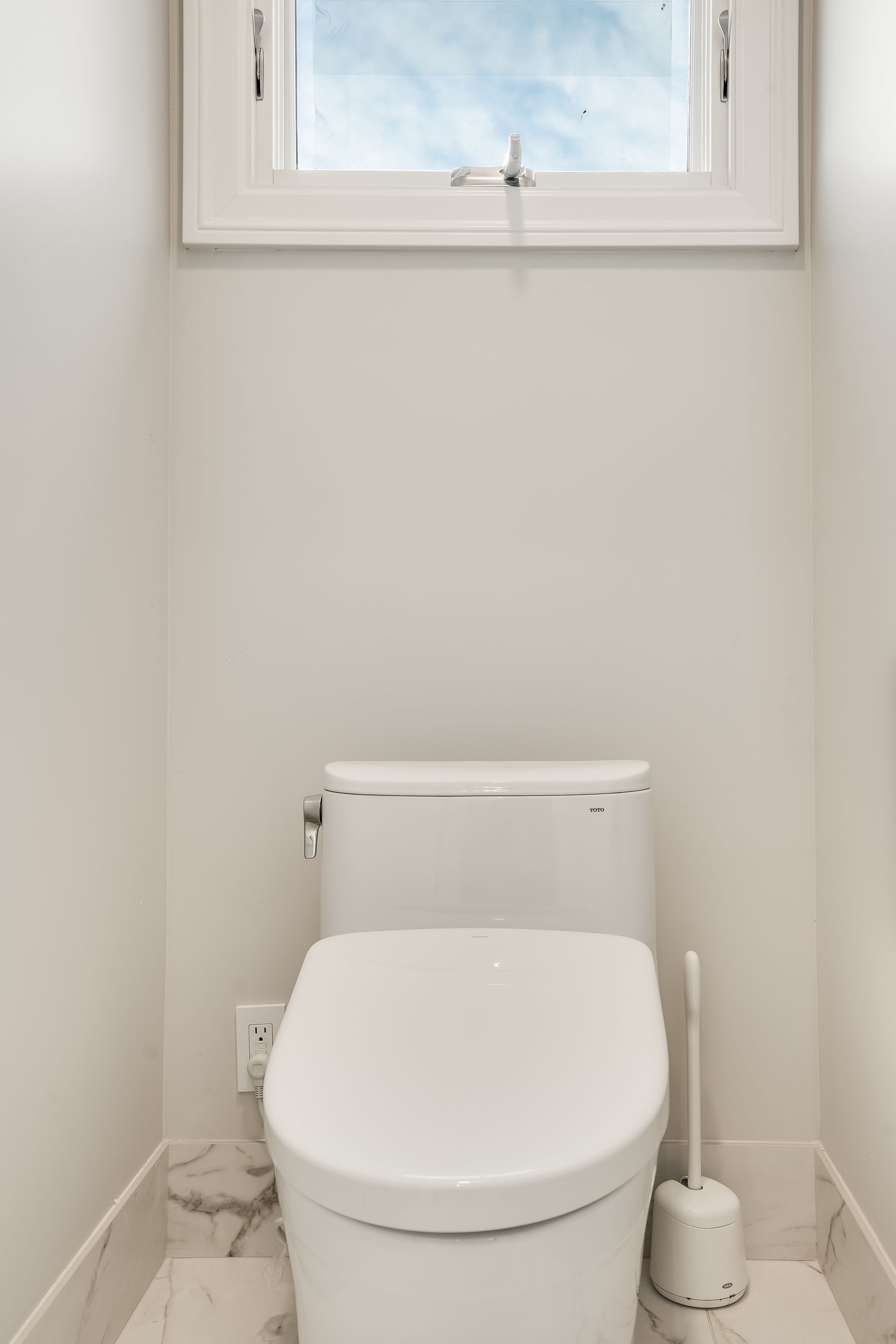 Small bathroom with a white toilet beneath a window and a toilet brush holder on the right.