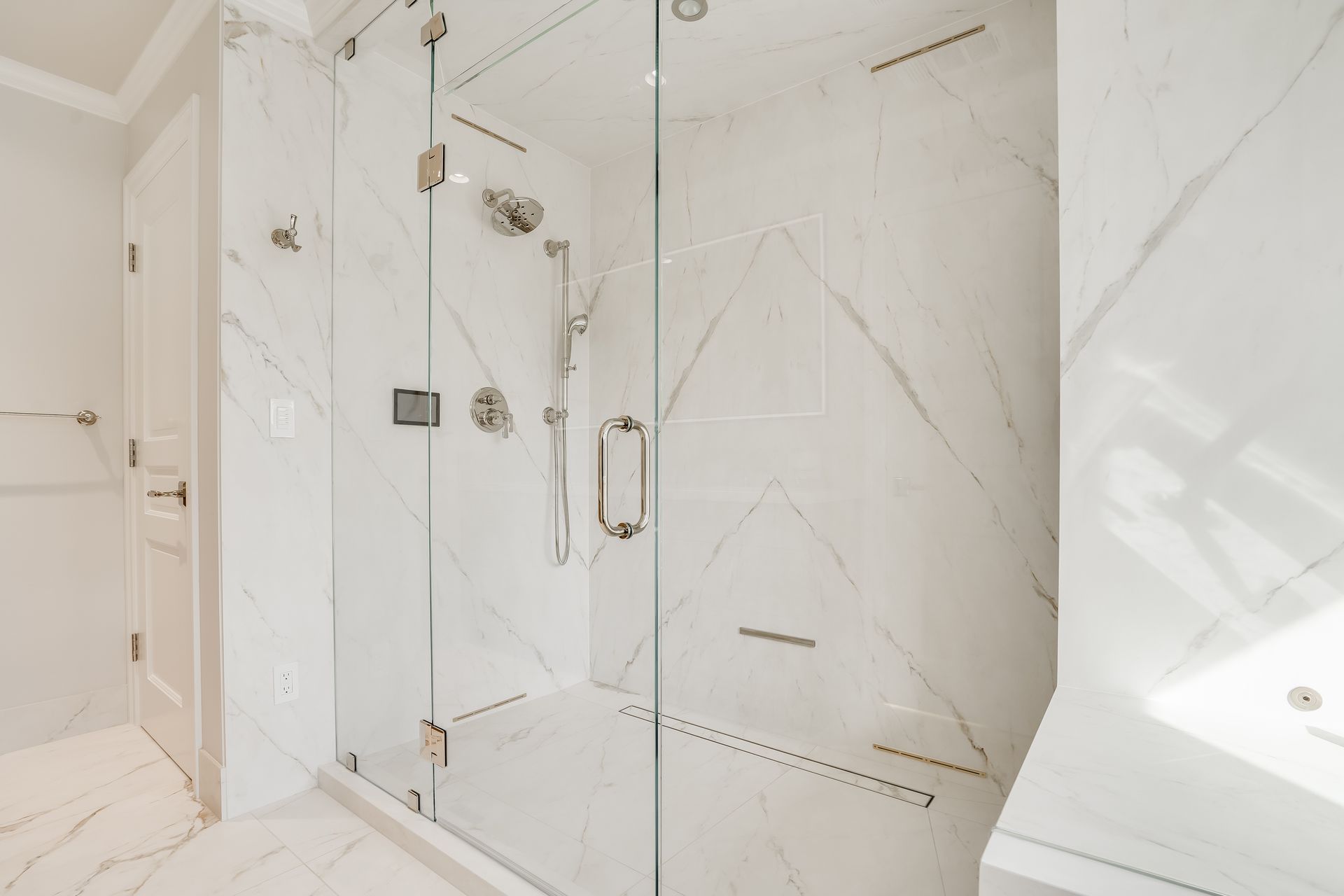 Bright white marble walk-in shower with glass door and chrome fixtures in a modern bathroom