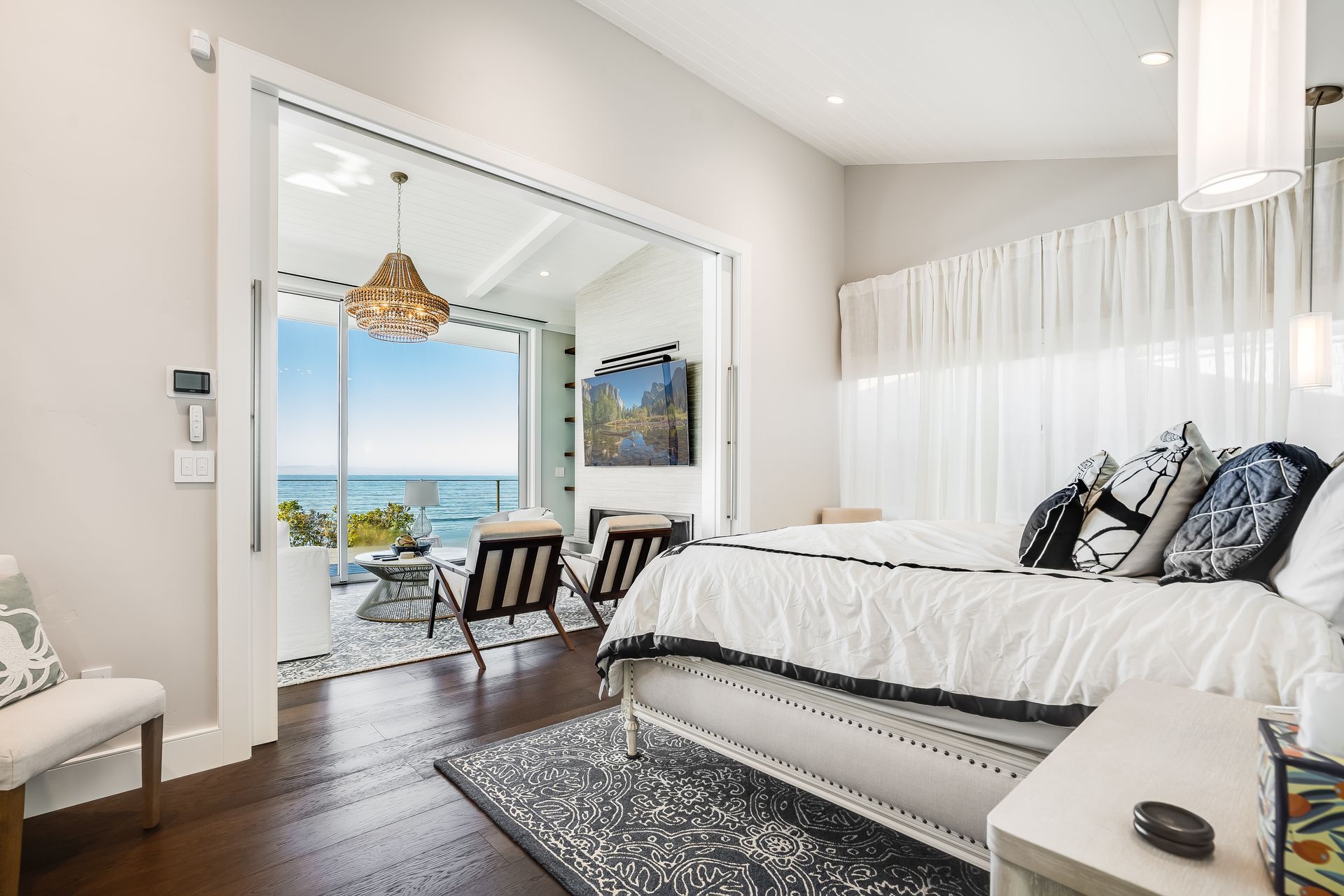 Bedroom with ocean view, featuring a bed, chairs, and open glass doors to a balcony.