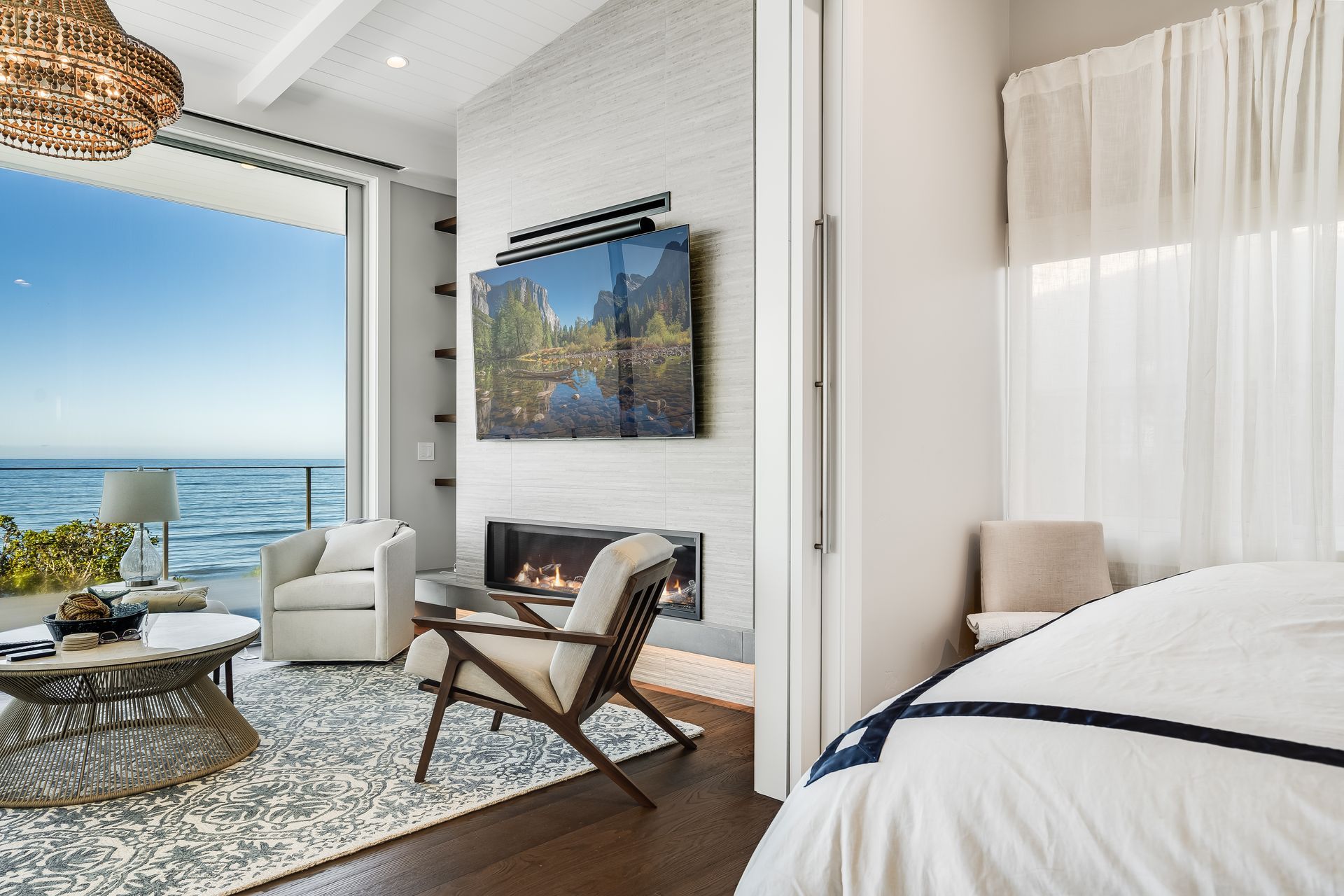 Bedroom with ocean view, fireplace, and modern furniture; bright, airy space with white and wood tones.