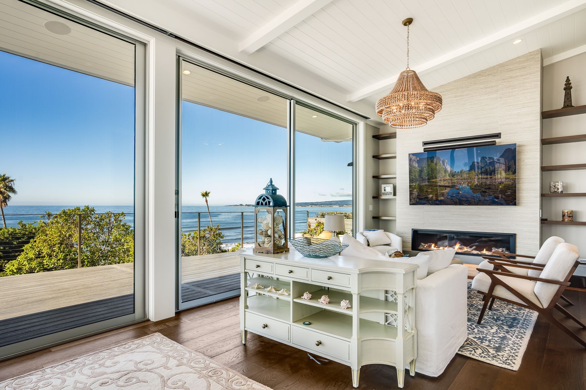 Living room with ocean view through large sliding doors, white walls, chandelier, fireplace, and shelves.