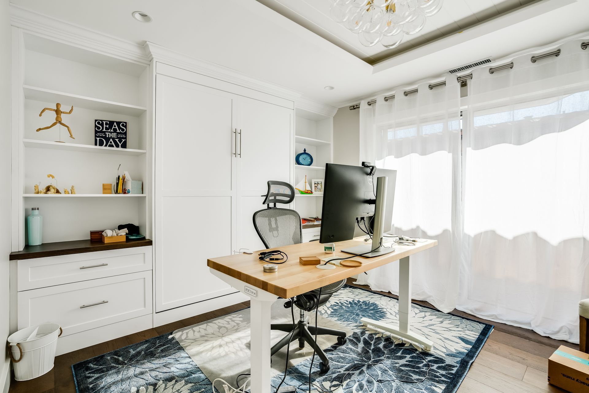 Home office with white built-ins, desk with large monitor, and a patterned rug.