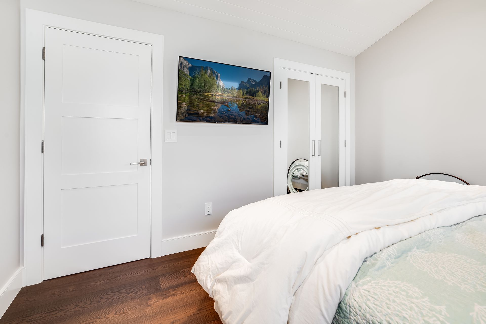Bedroom with bed, TV, two doors, and light gray walls.