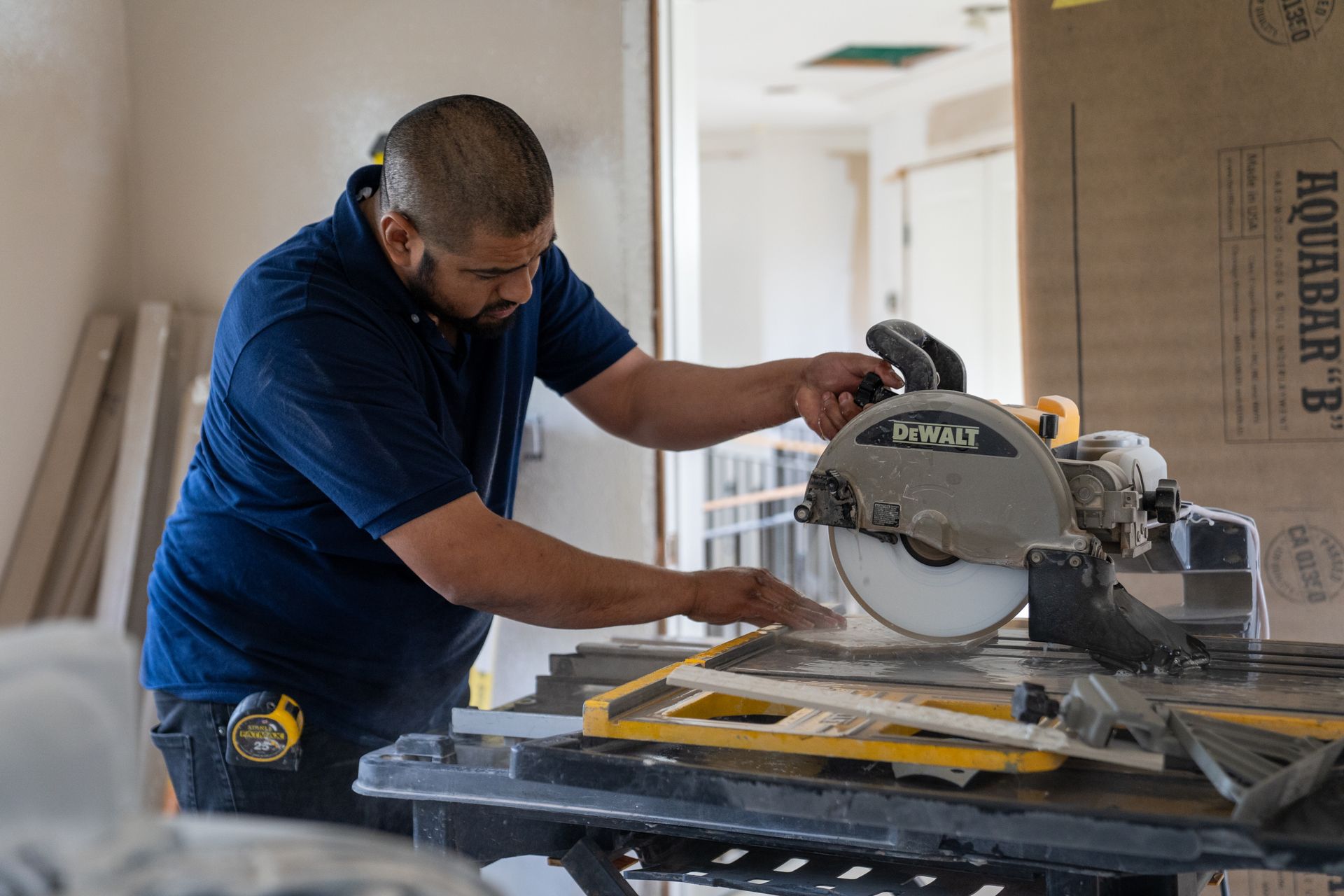 Man in blue shirt using a circular saw to cut a tile, indoors.