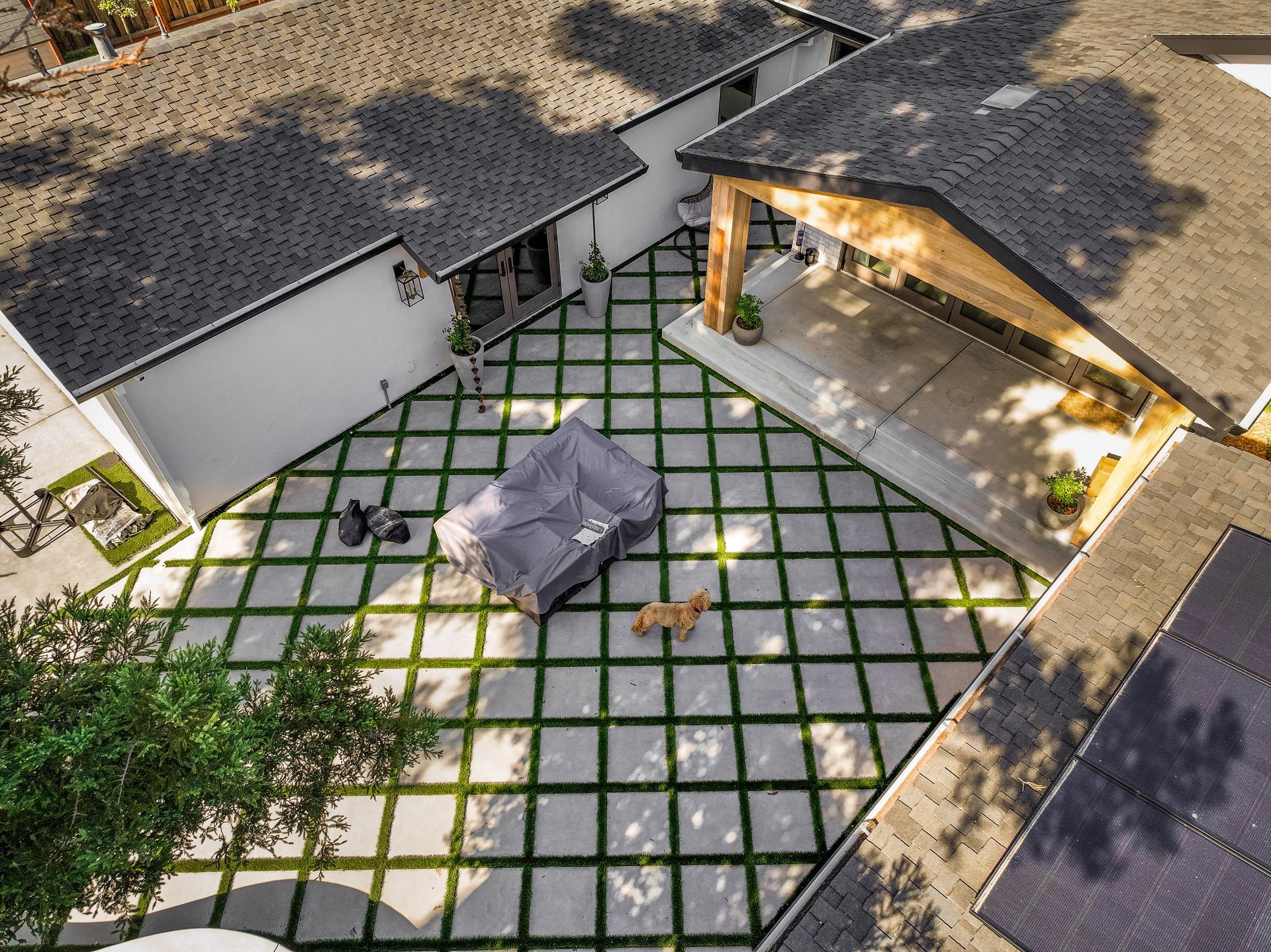 Aerial view of a courtyard with square pavers, a covered fire pit, and a pergola beside a white building.