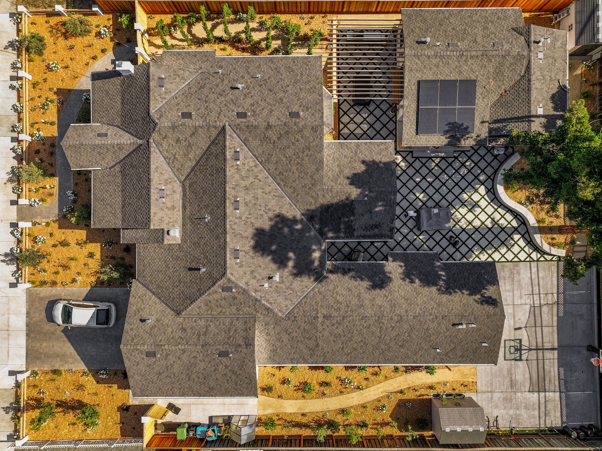 Aerial view of a house with a gray roof, driveway, patio, and surrounding landscaping.