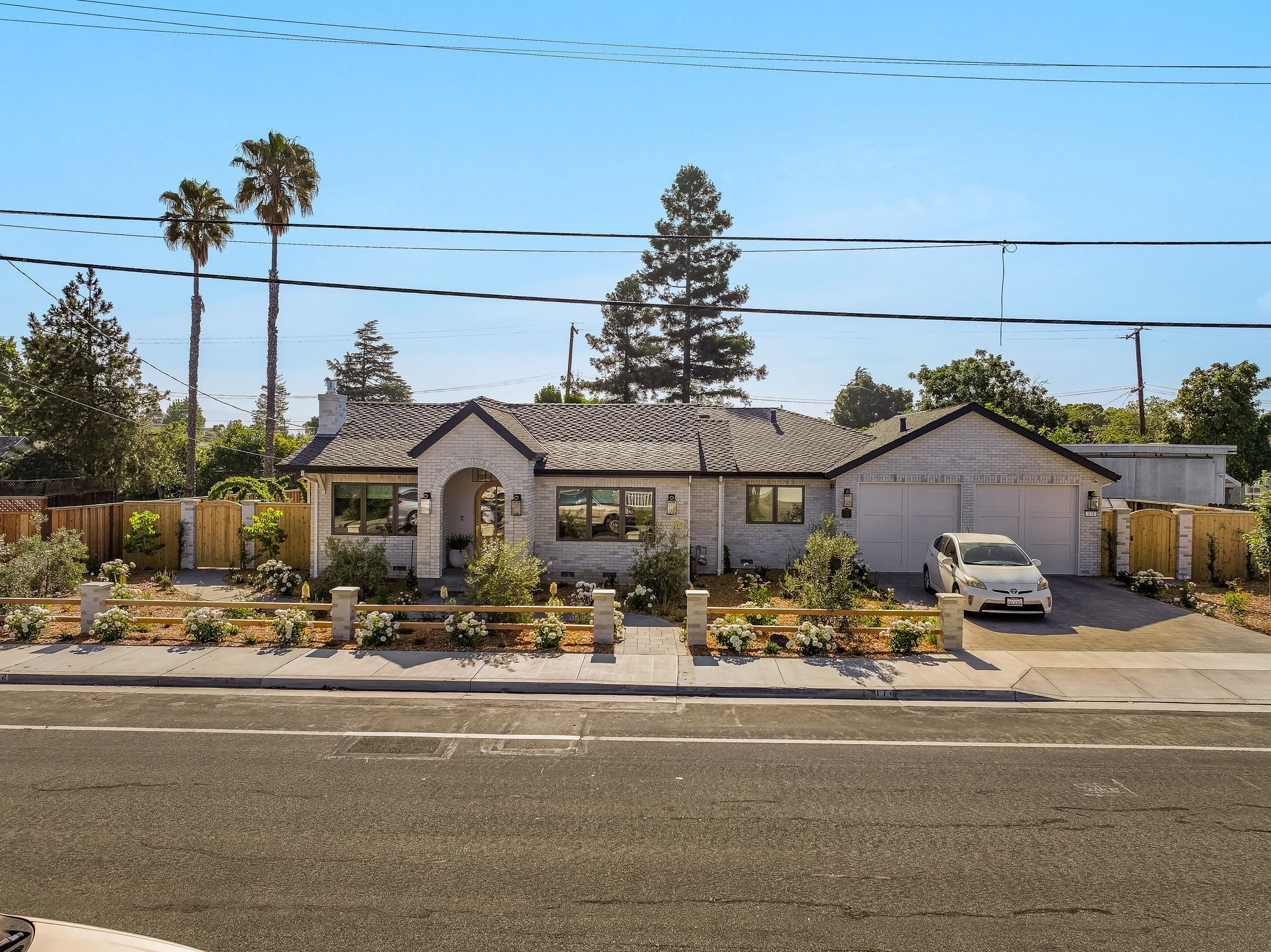 Single-story suburban house with a front yard, palm trees, and a parked car under a clear blue sky