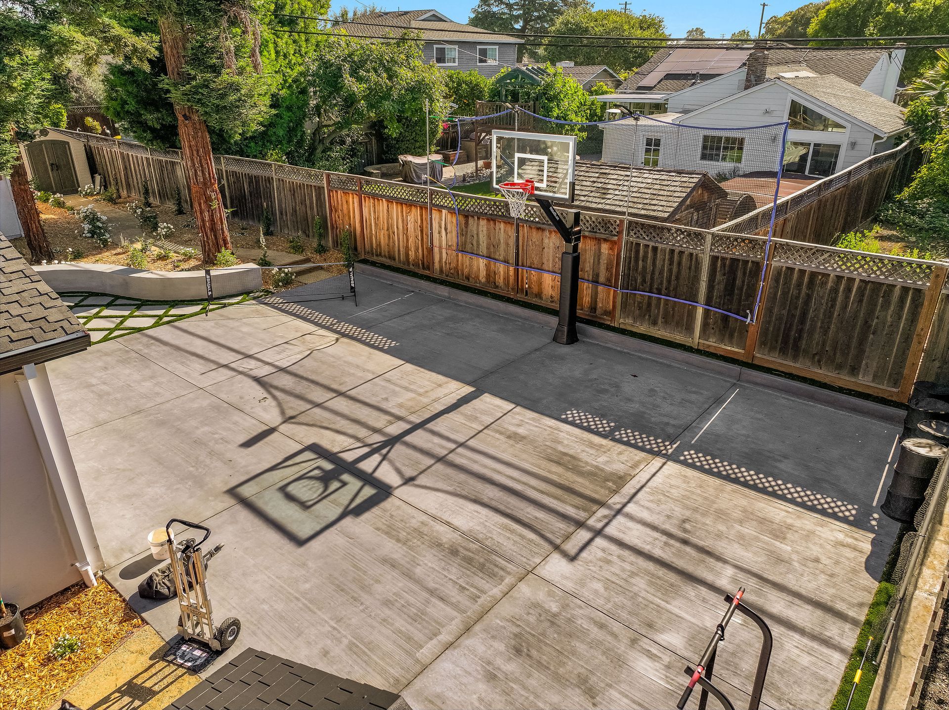 Backyard basketball court with hoop, wooden fence, and surrounding trees and houses