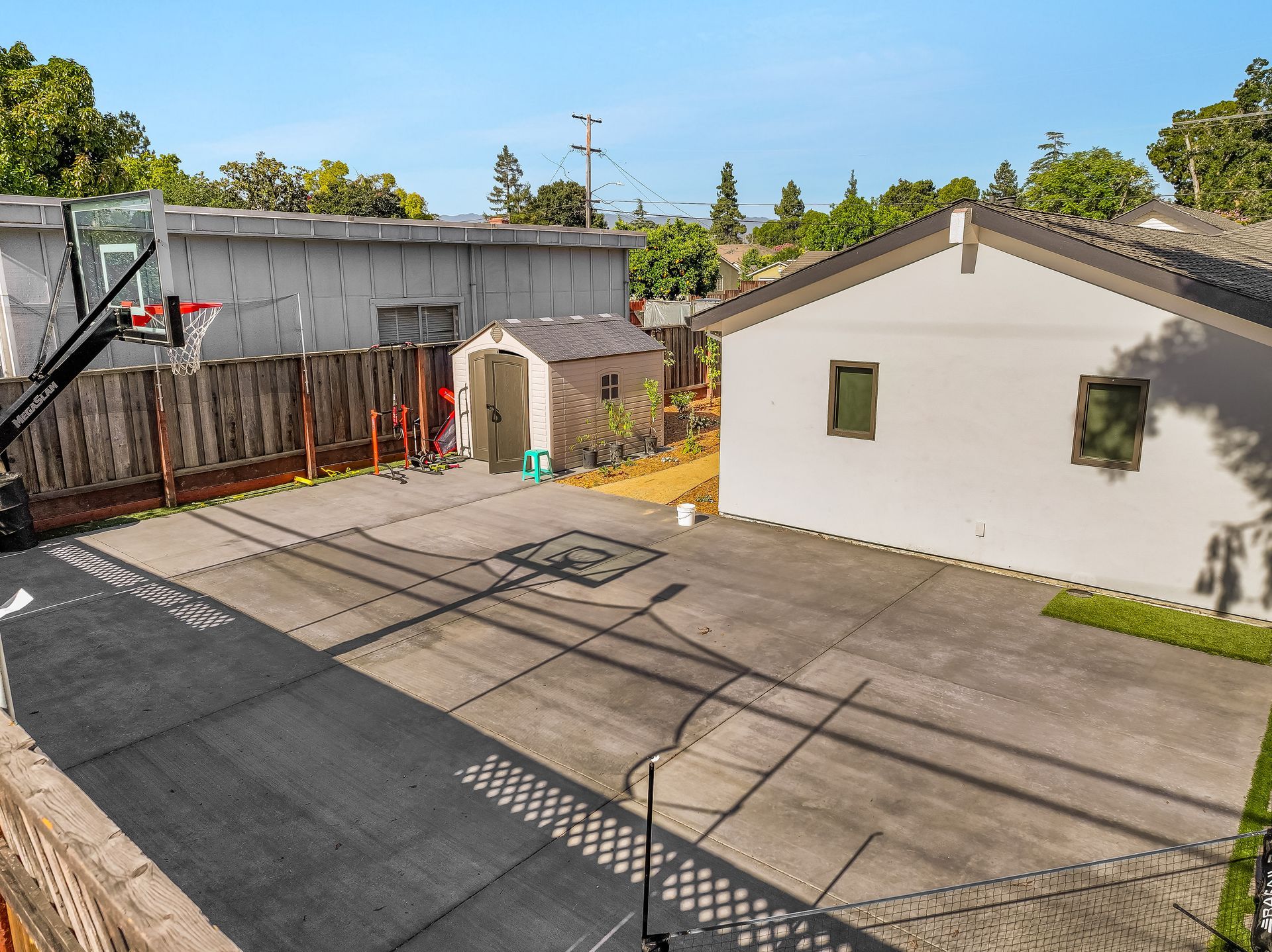 Backyard concrete driveway beside a white garage and fenced area under a clear blue sky