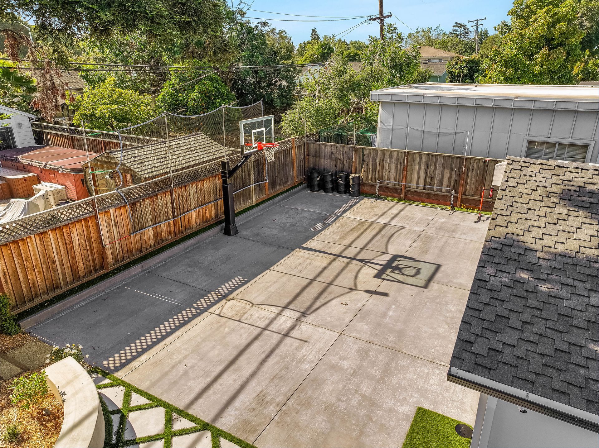 Backyard concrete court with a hoop, wooden fence, and surrounding greenery