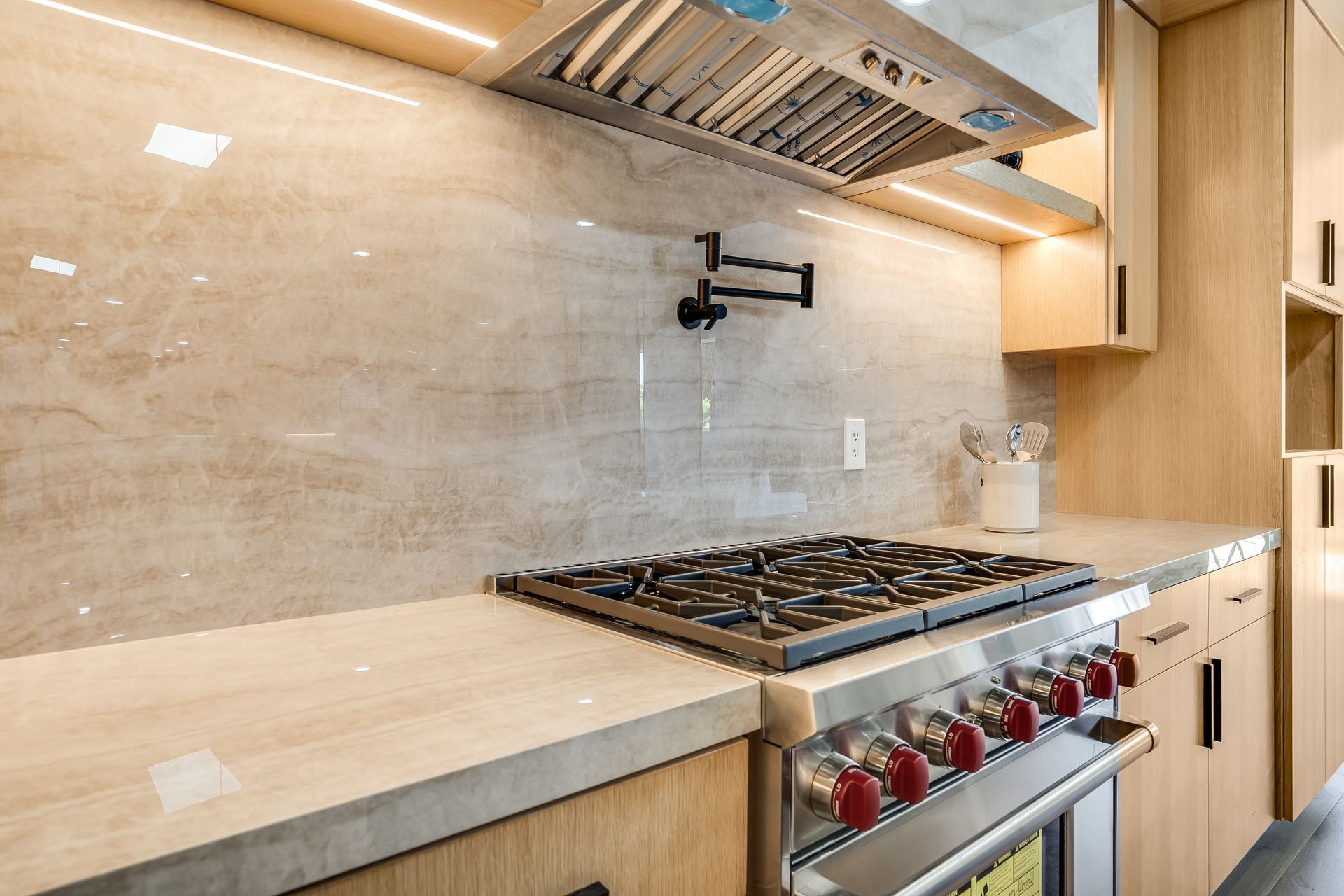 Modern kitchen with gas stove, stainless steel oven, beige backsplash, and range hood