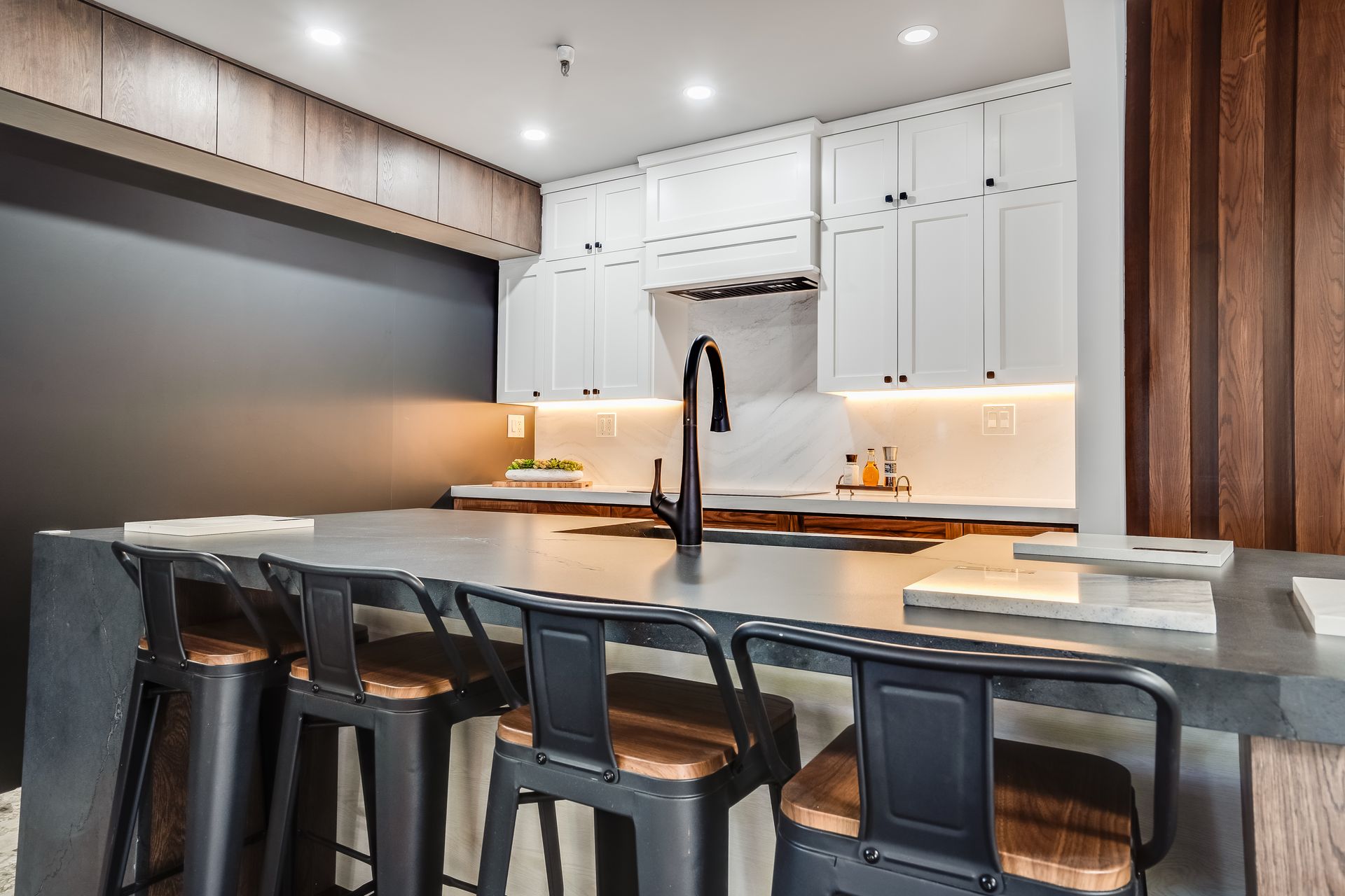 Modern kitchen with white cabinets, black island, bar stools, and warm under-cabinet lighting