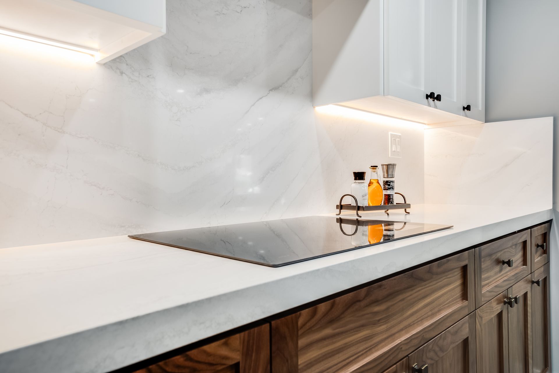 Modern kitchen countertop with built-in cooktop and small condiment bottles under white cabinetry