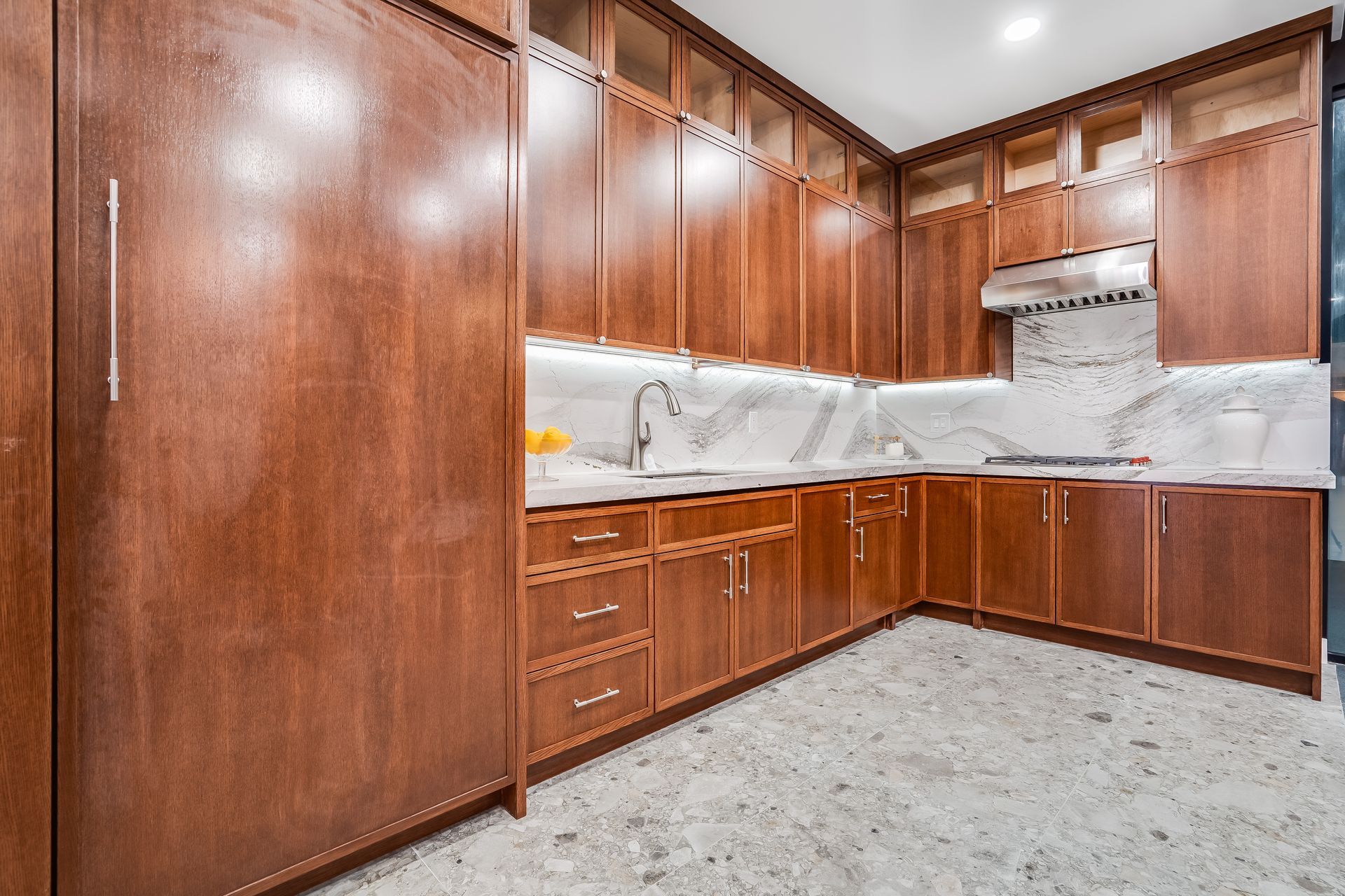 Wood-paneled kitchen with white marble counters and built-in cabinets around a corner sink.