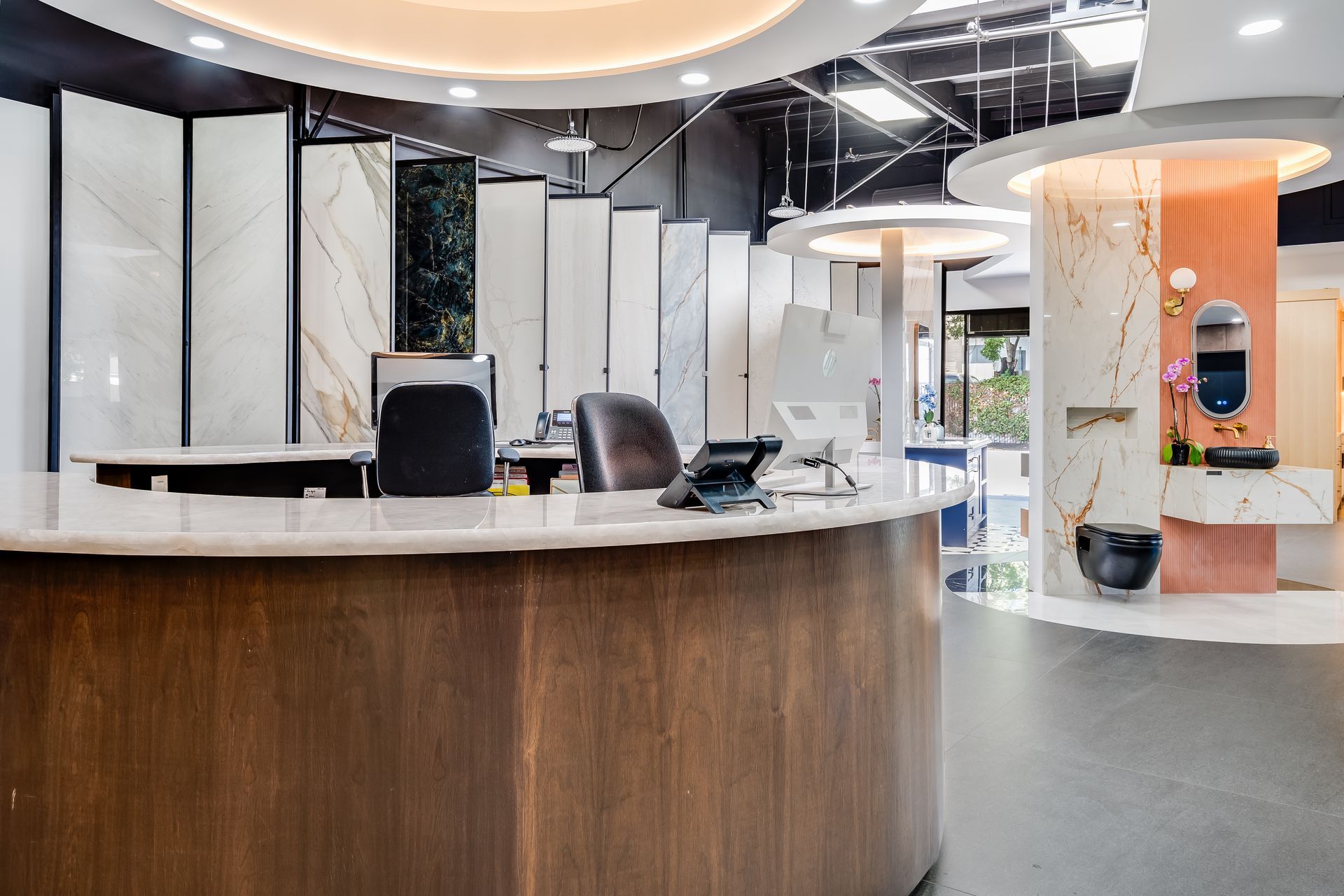 Modern office reception area with a curved wooden desk, white walls, and lounge seating