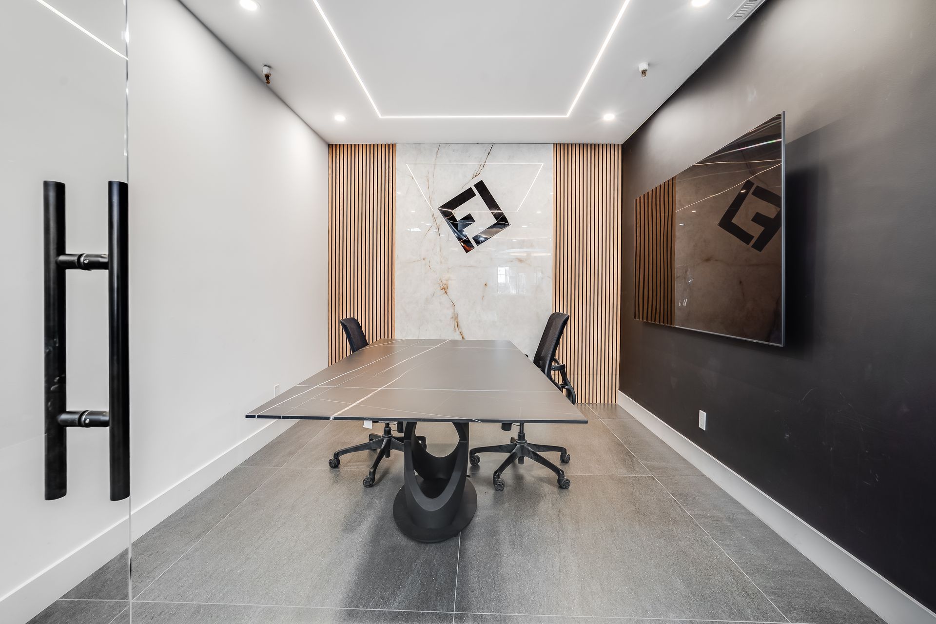 Modern conference room with long glass table, black chairs, and wall-mounted TV in a minimalist interior