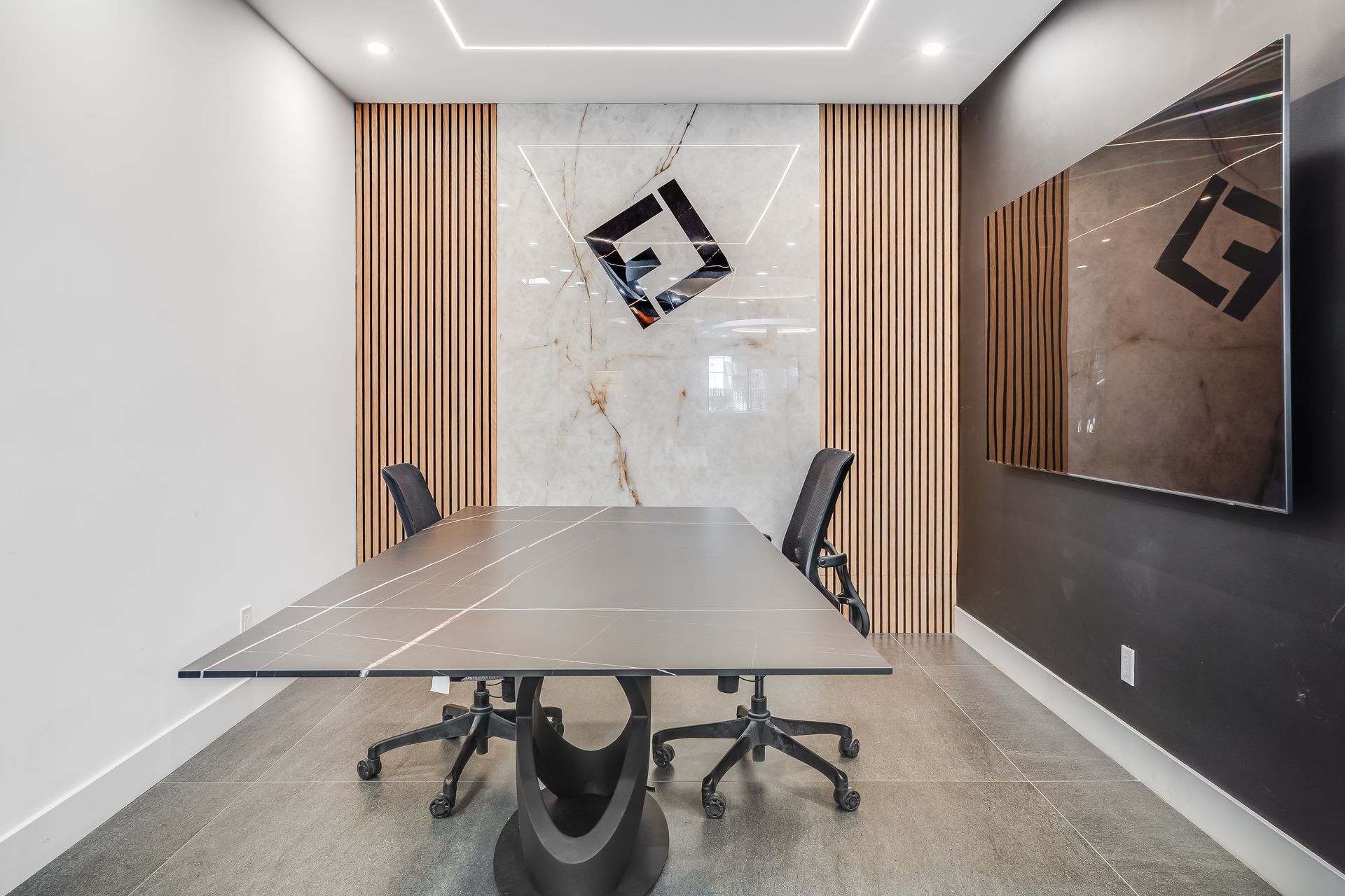 Modern conference room with marble table, black chairs, wood slat wall, and wall-mounted screen