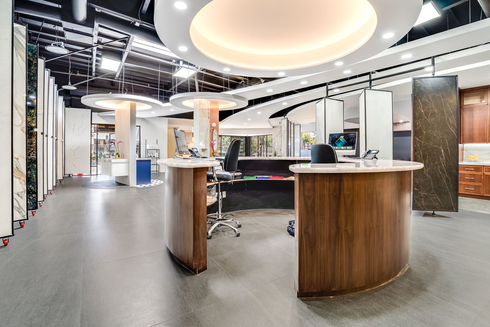 Modern office reception area with curved wooden desks, open workspace, and circular ceiling lights